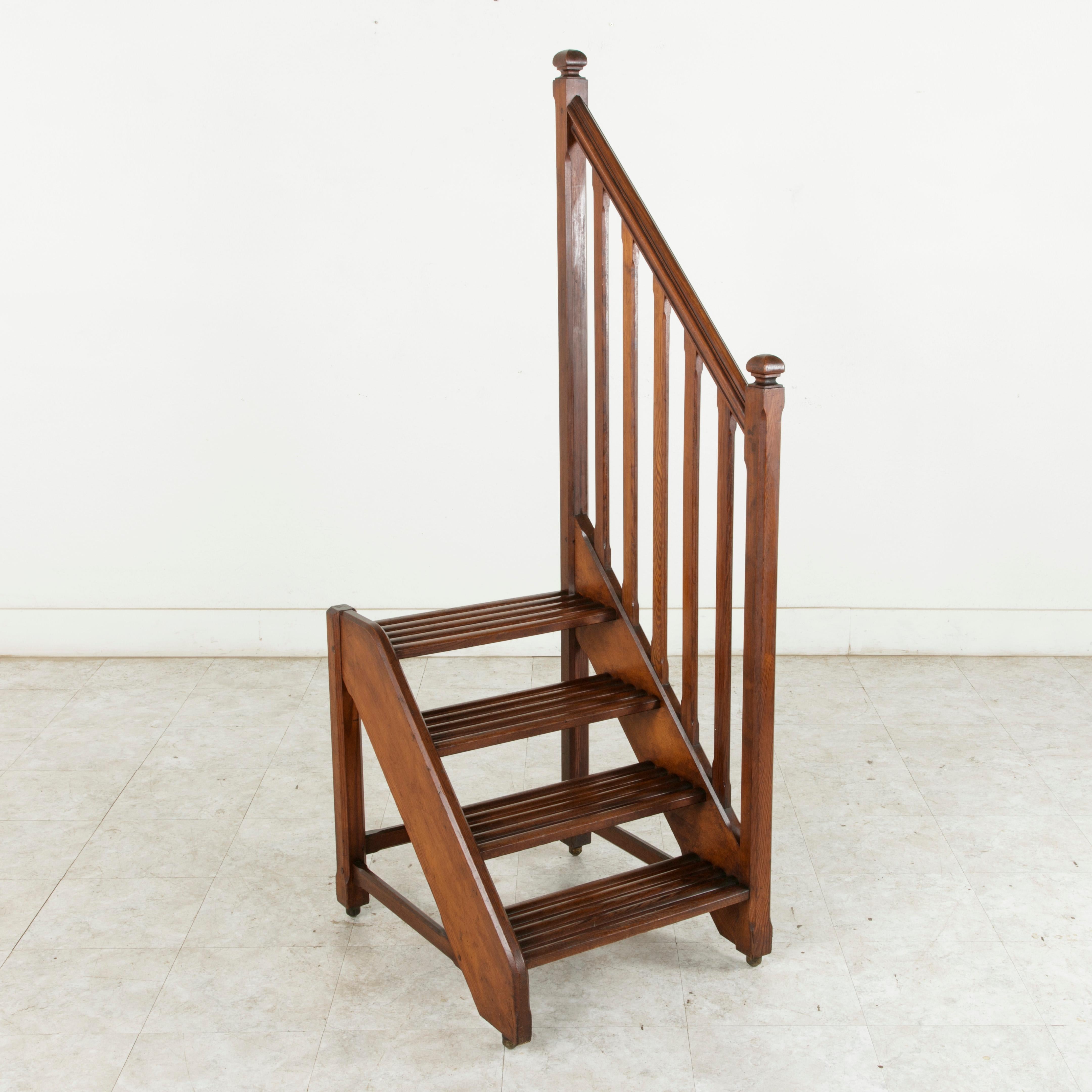 This handsome French library ladder from the turn of the 20th century is constructed of hardwood heart pine and features a hand rail on the right side, providing stability when climbing for hard-to-reach books. Each of its four steps is formed by