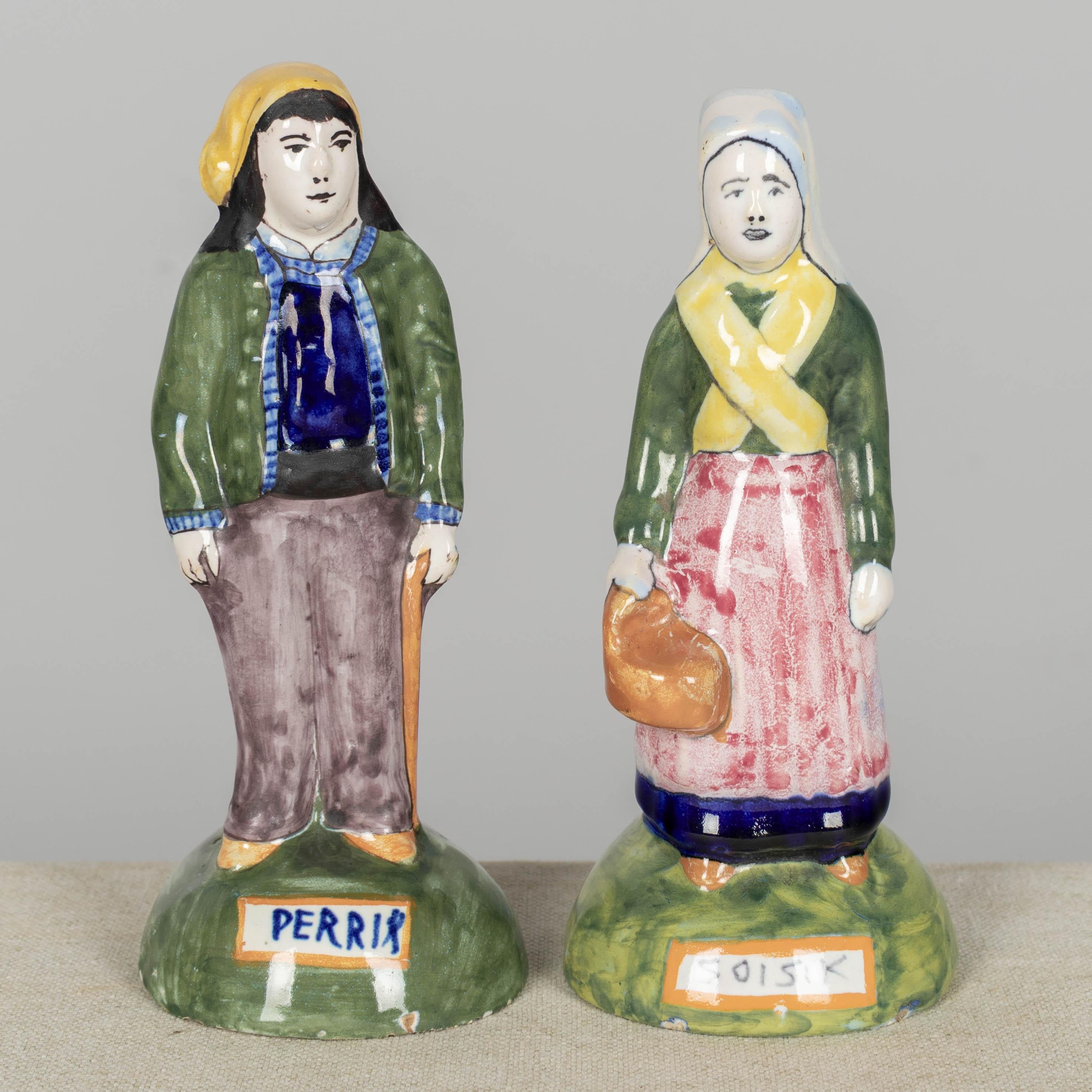 A pair of late 19th century French Henriot Quimper faience statues, or figurines, of Perrik and Soisik. Polychrome enameled earthenware, hand-painted in green, yellow, blue and red. These Breton figurines are part of a tradition of portraying