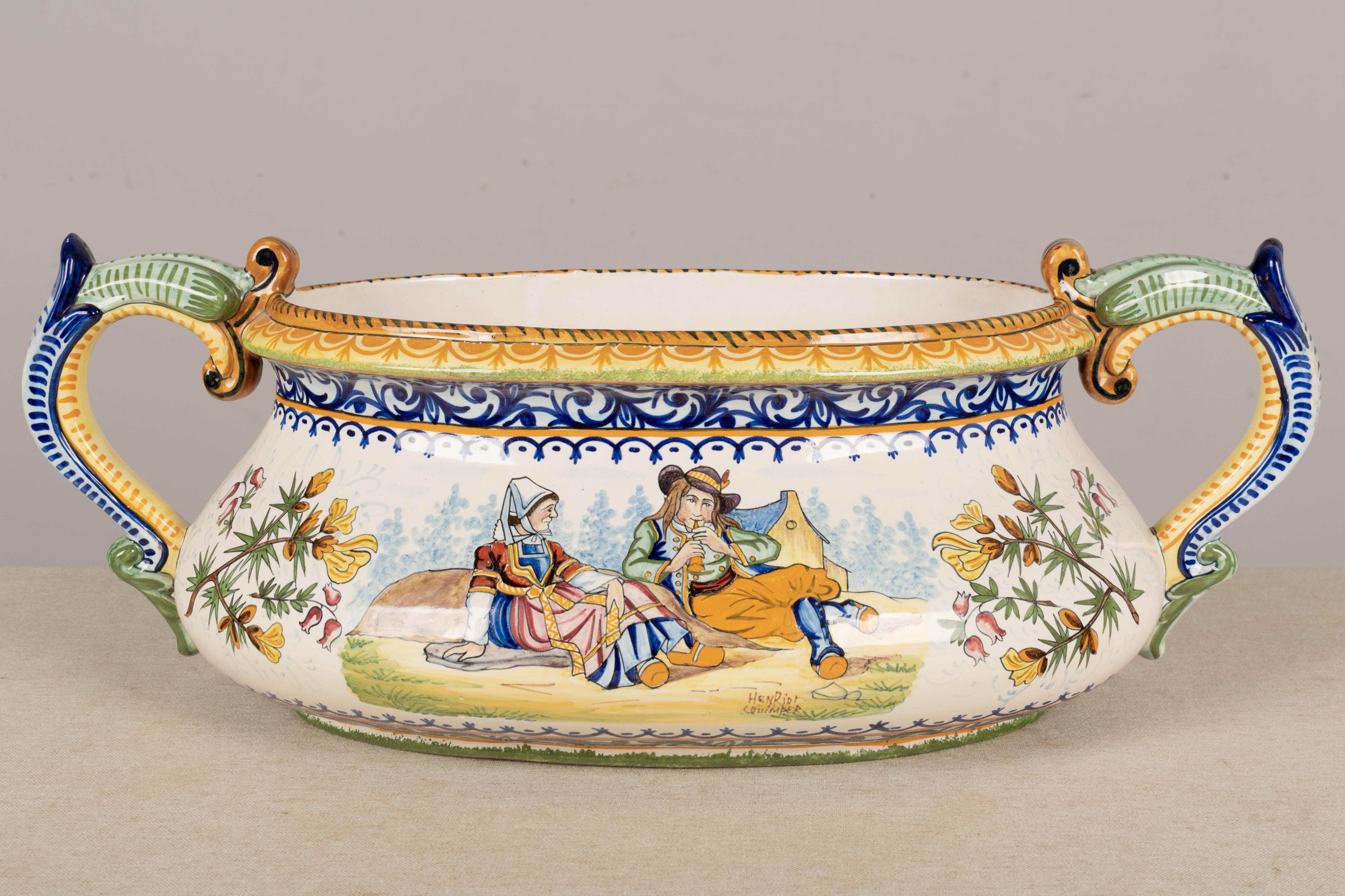 A French Henriot Quimper faience oval jardiniere, or planter, with large handles. Hand-painted decoration, one side depicting a man and woman in traditional dress, the other side with the Bretagne crest, each flanked by sprigs of flowers. Bold