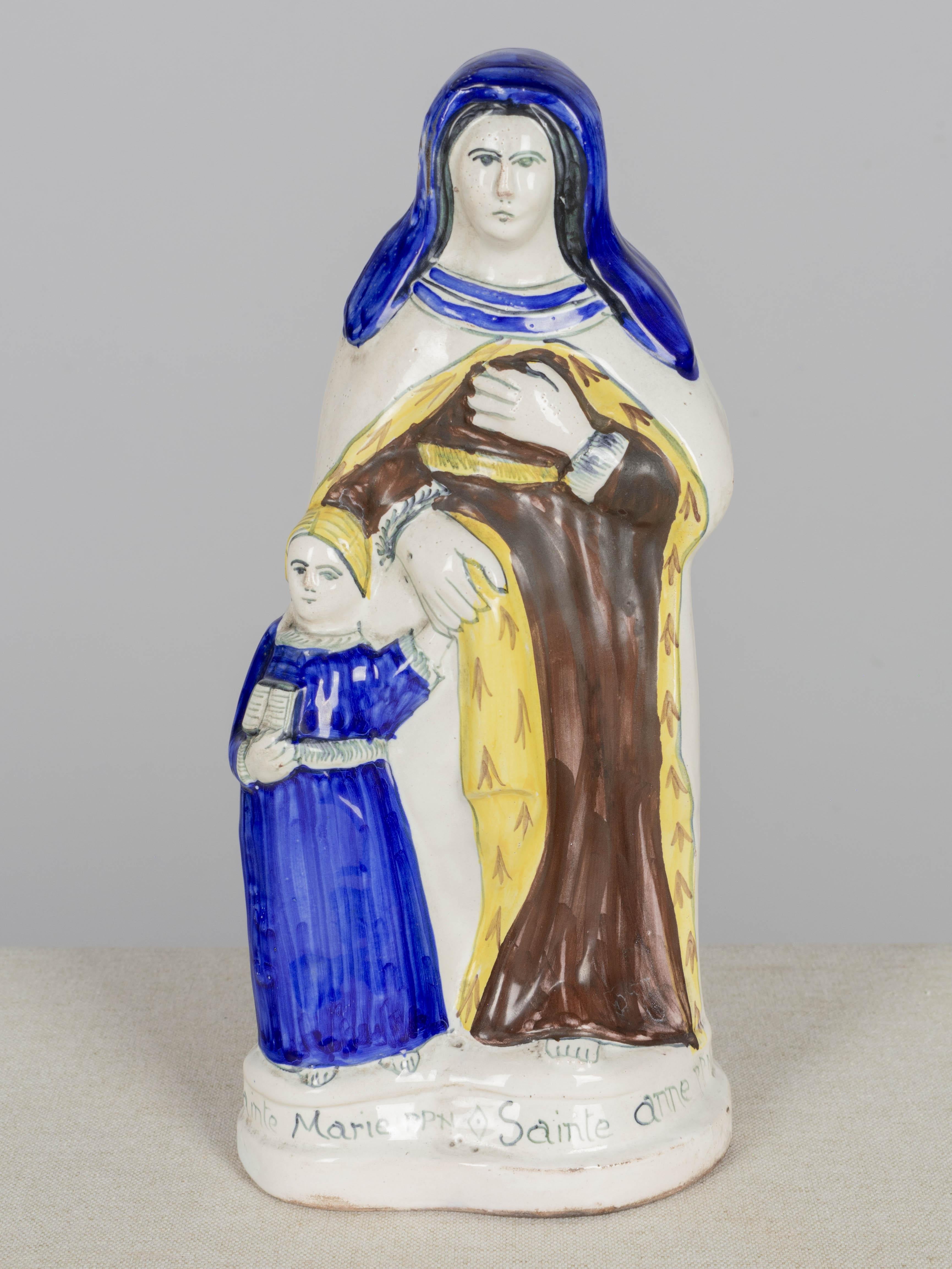 Estatua francesa de loza de Santa Ana y la Virgen María joven, de Henriot Quimper. Loza esmaltada policromada, pintada a mano en azul, marrón y amarillo. Titulado en la base y marcado en la parte inferior: Henriot Quimper, Francia. Alrededor de