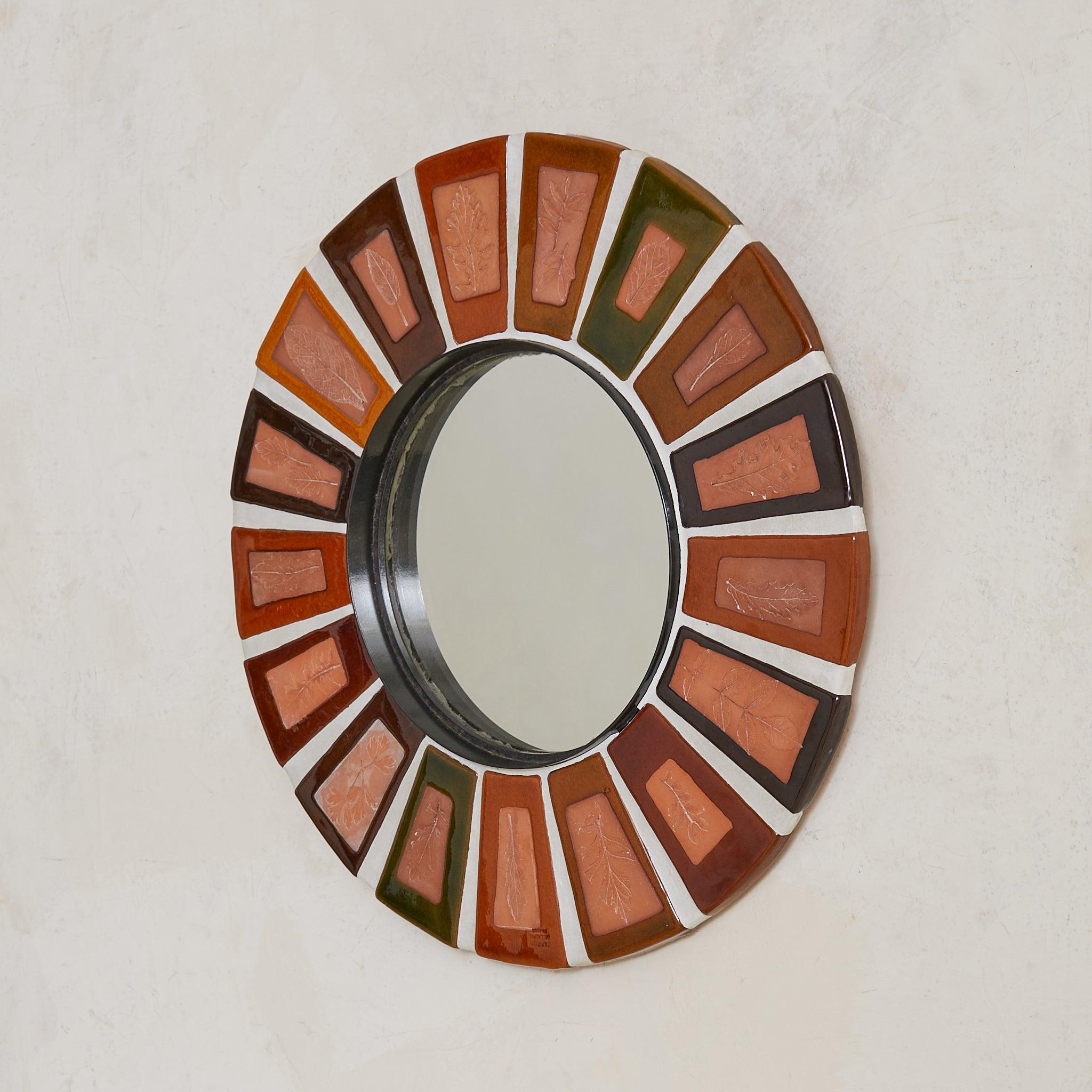 Espejo de pared de cerámica francesa de los años 70, de Roger Capron, con sus icónicos azulejos Herbier, cada uno con una impresión de hoja, que captura las finas venas y bordes de la flora silvestre en relieve de terracota. El marco redondo alterna