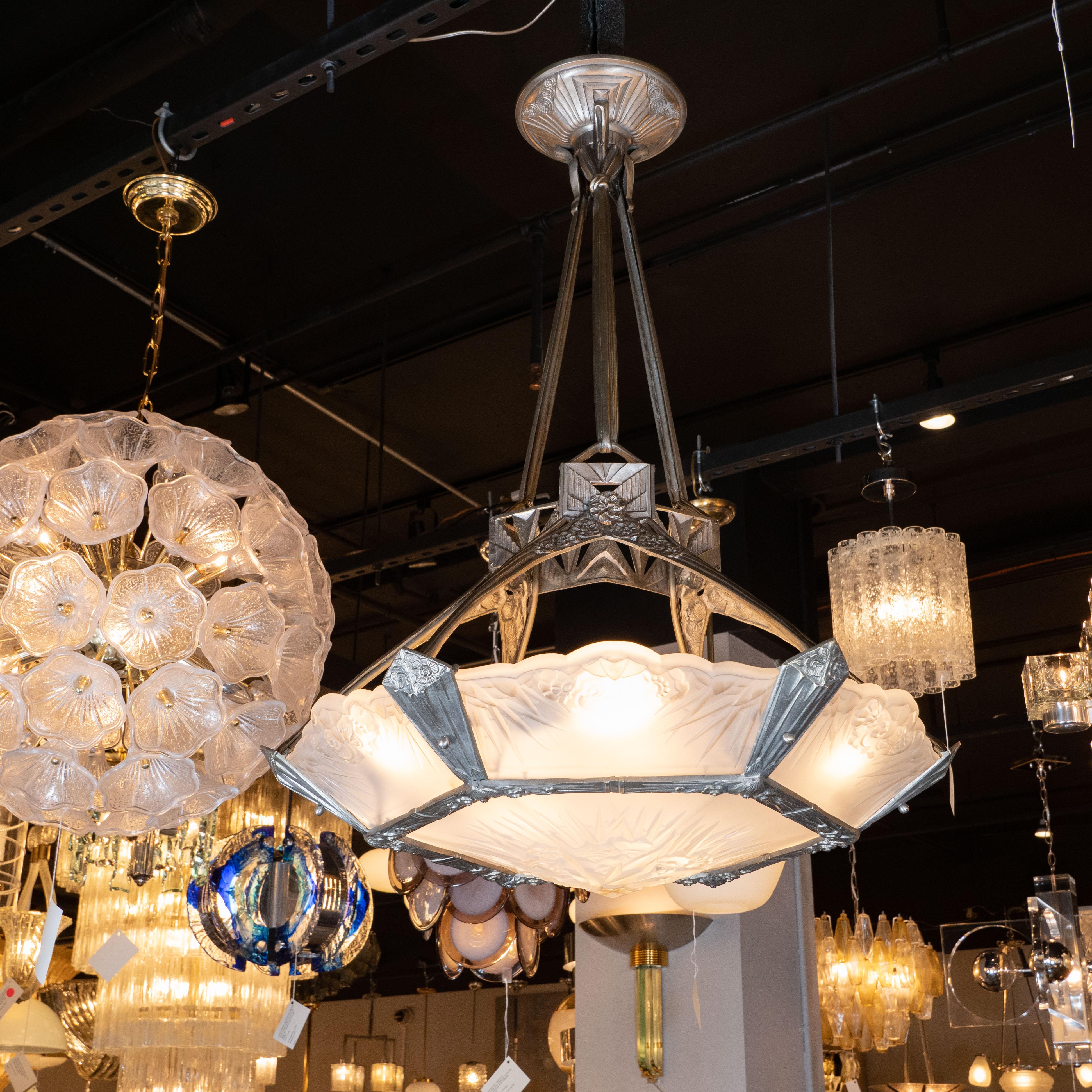 This elegant and sophisticated High style Art Deco Chandelier was realized in France, circa 1930. It features a hexagonal silvered bronze frame with stylized cubist geometric designs, including sunburst and cloud motifs. The frame supports six side