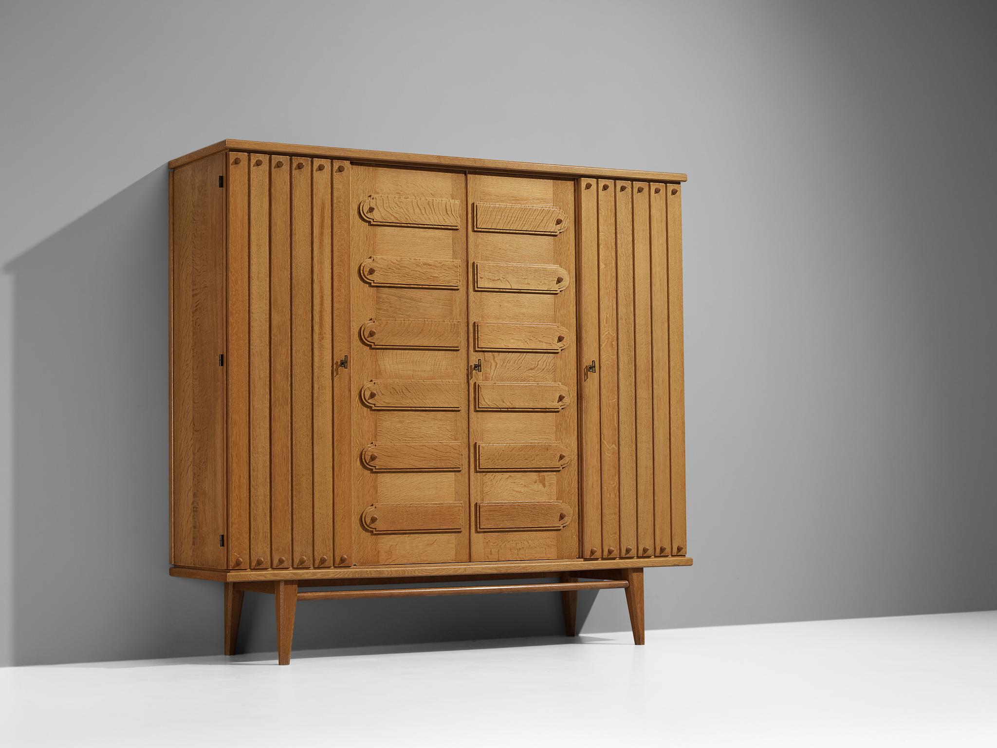 Wardrobe, oak, France, 1960s.

This elegant armoire has a considerable size which provides great storage space. The door panels are rhythmically structured composed of wood carvings. The corpus is supported by tapered legs, which are