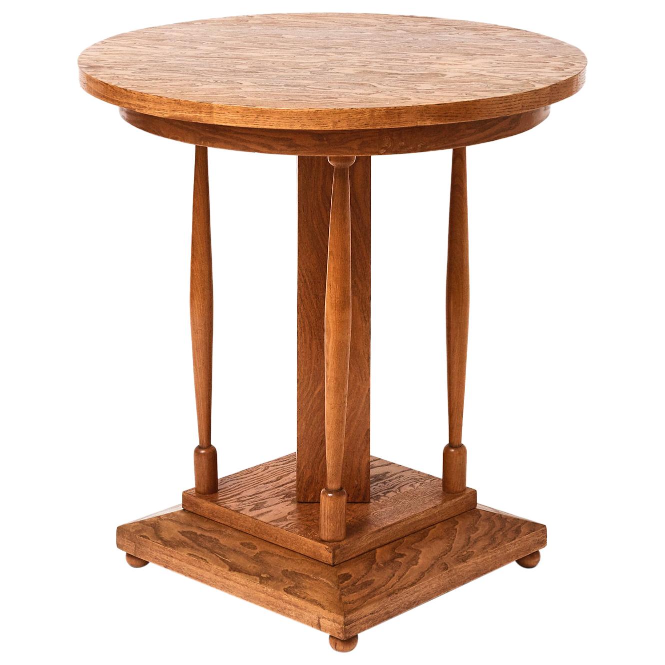 A French figured oak veneer pedestal table, circa 1920, the circular top above a square central pedestal and four turned supports, raised on a canted and square base.


