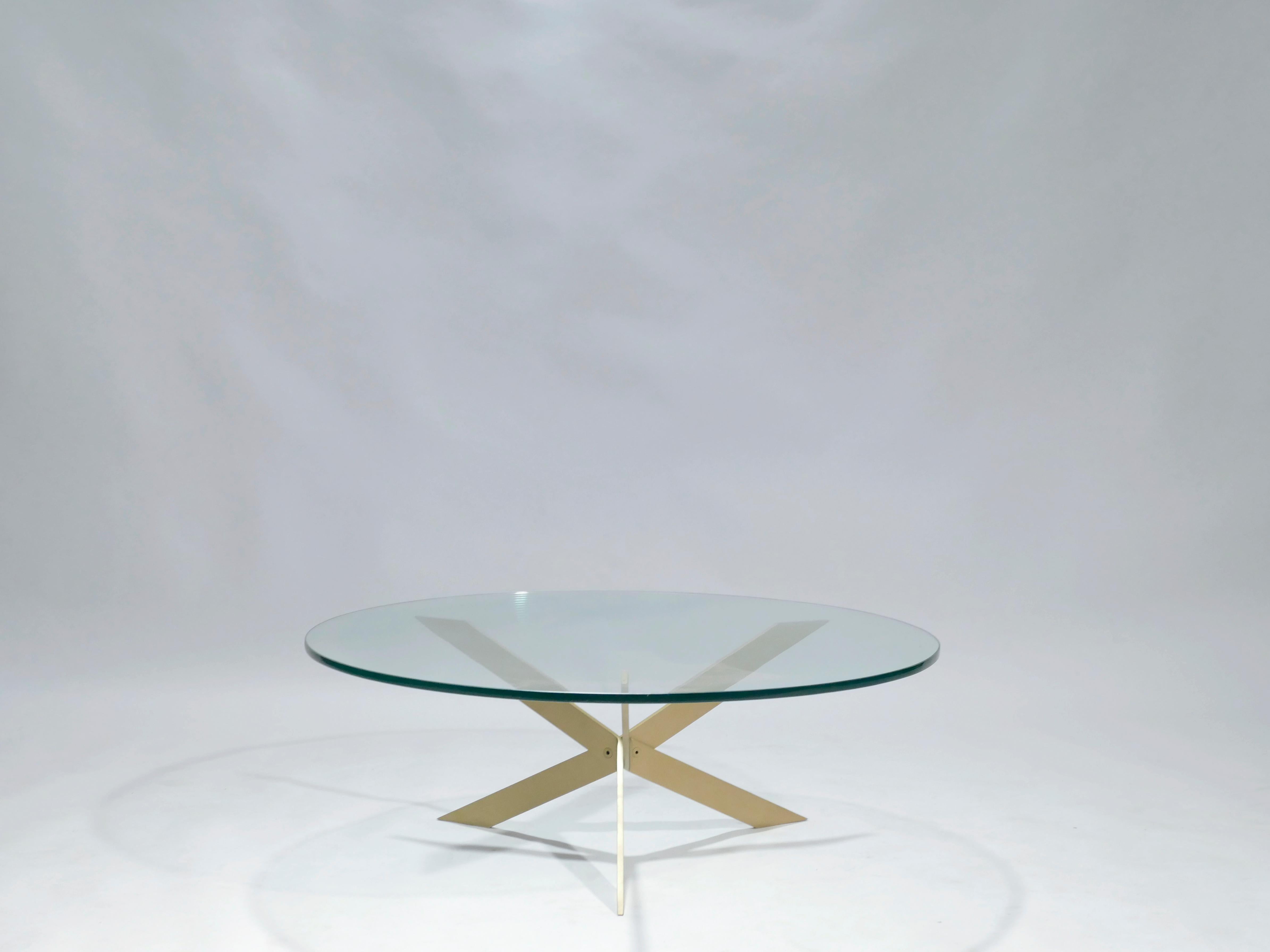 Three inventive brass structures serve as criss crossing legs in this Mid-Century Modern coffee table. Heavy, transparent glass is cut into a sleek circle to form the surface, allowing the intriguing arrangement of the legs, full of sharp angles, to