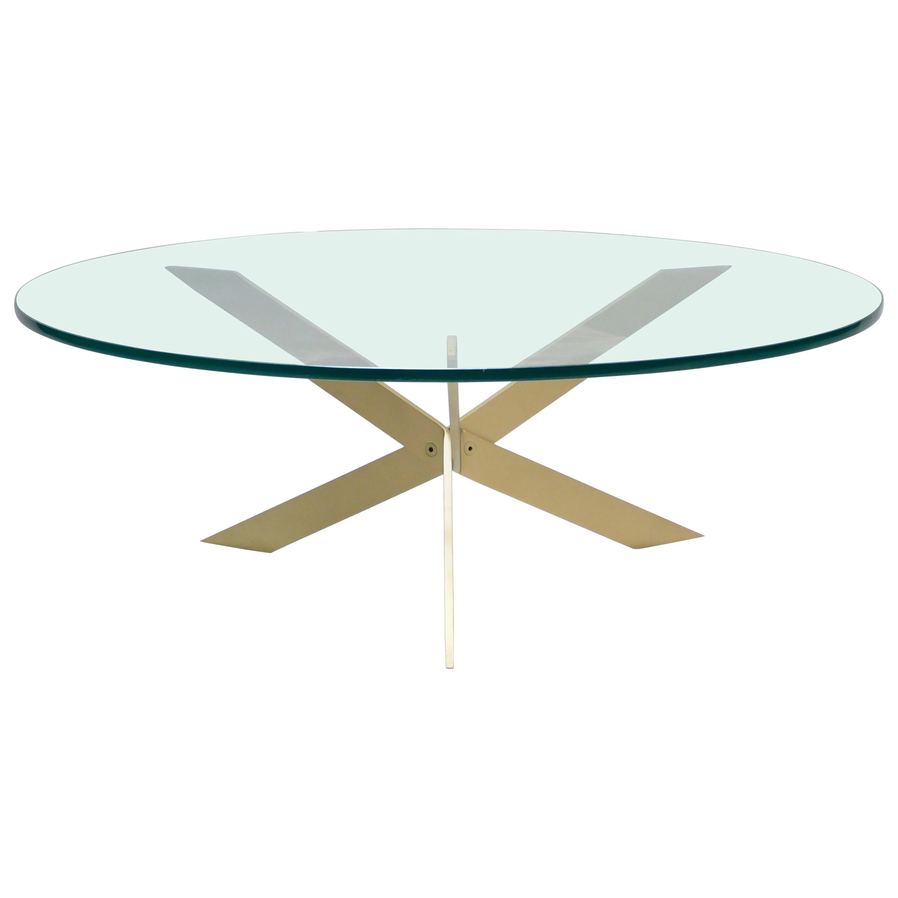 Trois structures inventives en laiton servent de pieds croisés à cette table basse moderne du milieu du siècle. Le verre lourd et transparent est découpé en un cercle épuré pour former la surface, ce qui permet à la disposition intrigante des pieds,