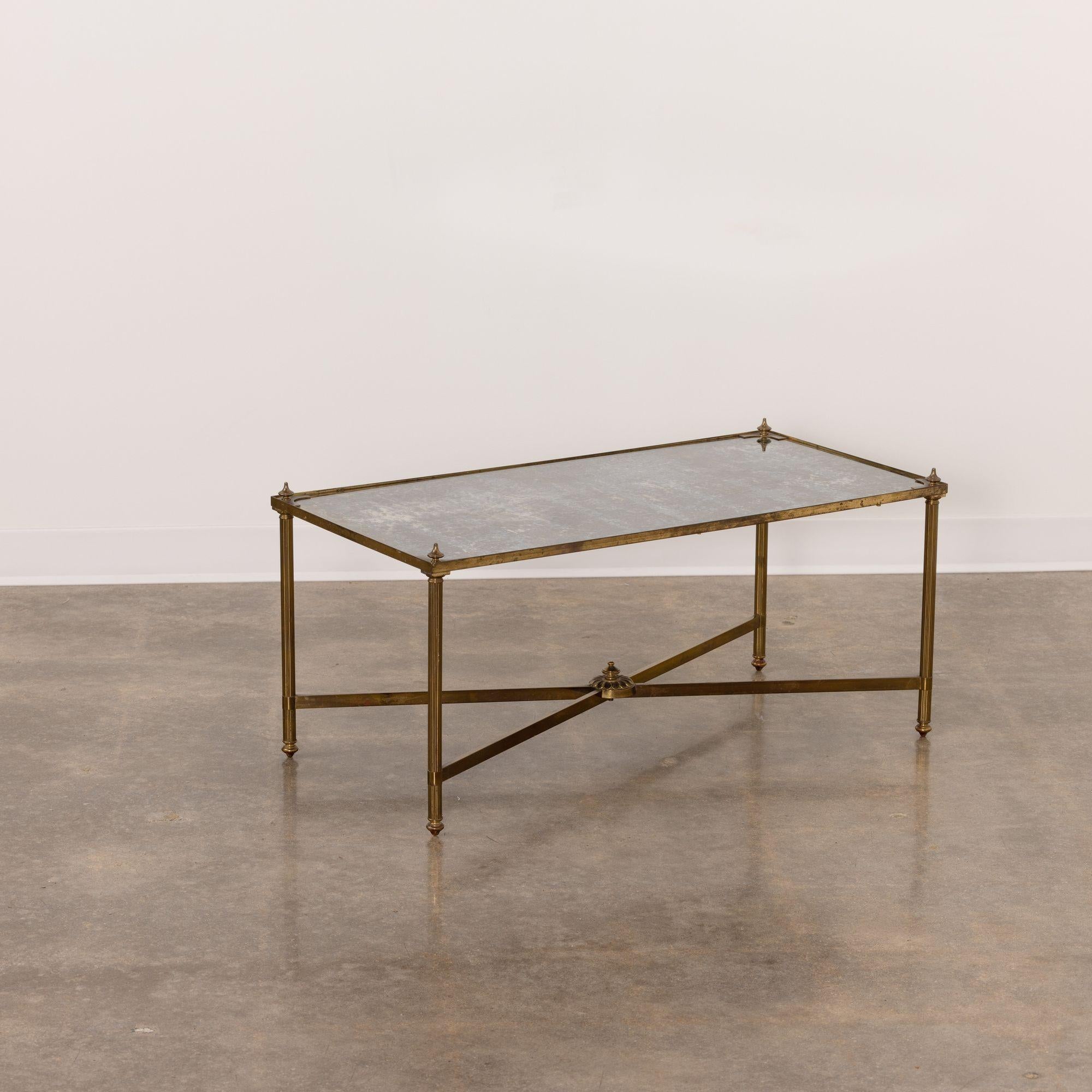 An elegant French brass cocktail table with an eglomisé top in the Hollywood Regency style, c. 1950. The beautiful rectangular table stands on four, fluted, brass legs joined by a cross stretcher base embellished with a finial.  The top is finished