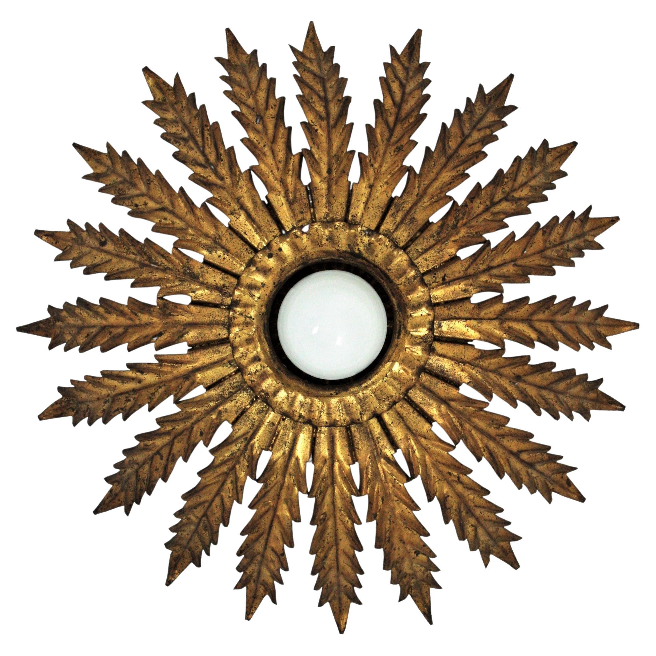 Elegant Hollywood Regency hand-hammered gilt iron sunburst flower light fixture / flush mount, France, 1940s-1950s.
This flush mount ceiling light features a wrought iron structure comprised by gold gilt iron scalloped leaves. The part surrounding