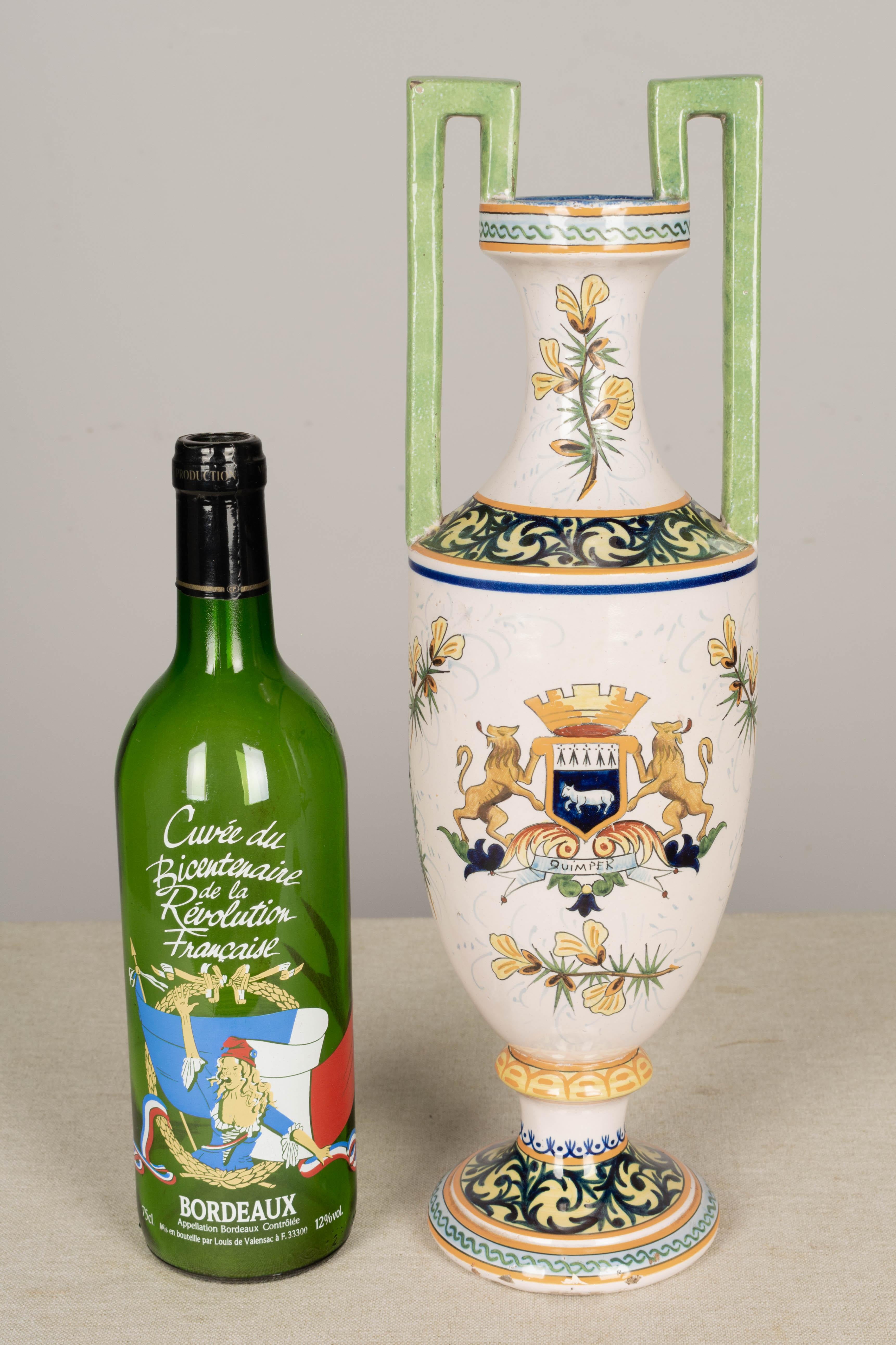 French faience vase signed HR Quimper, hand-painted with a man and woman depicted in traditional country attire in a pastoral setting. The reverse side has the Quimper coat of arms. Urn form with tall slender proportions and double handles painted