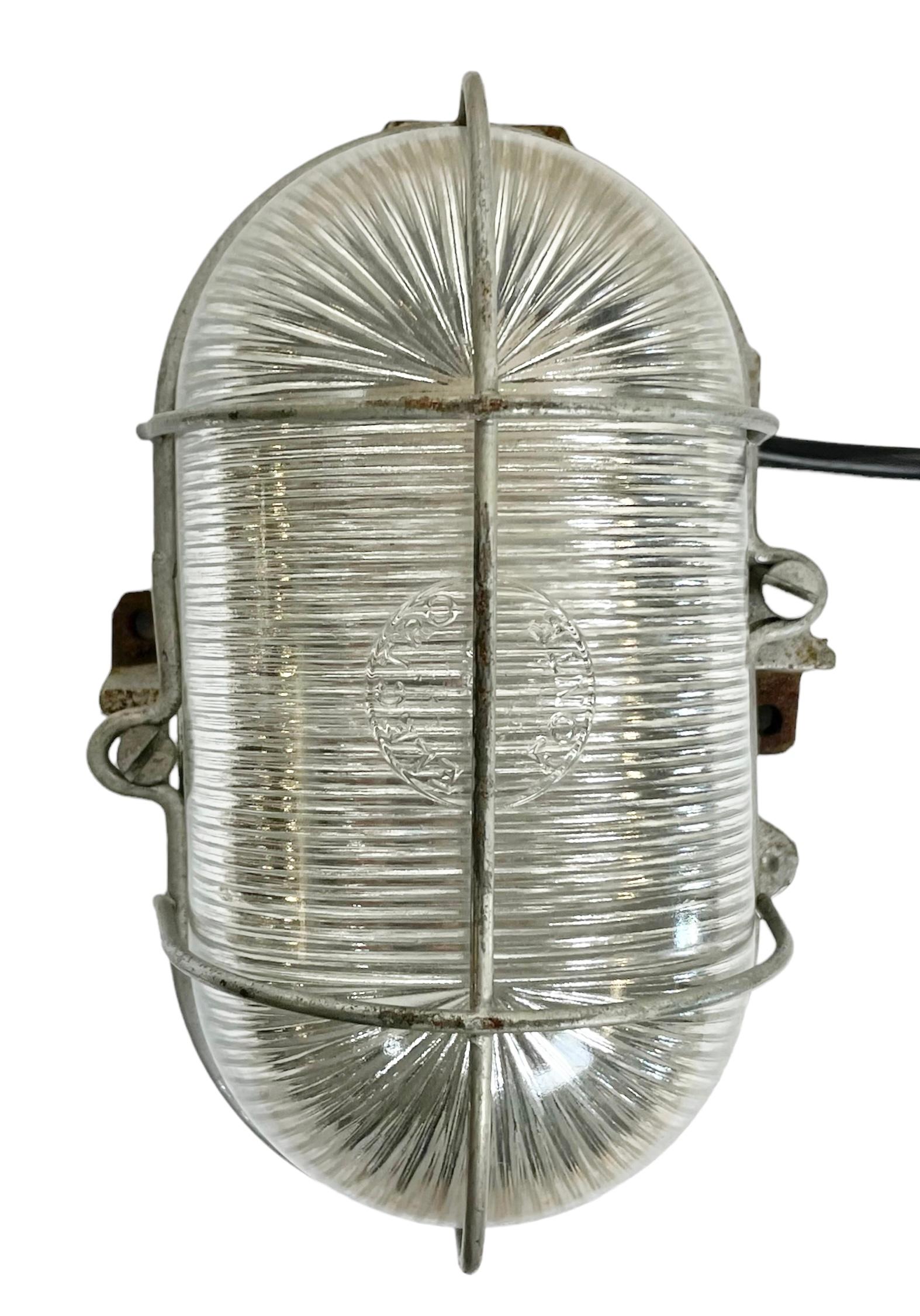 Applique industrielle fabriquée par Elecktro Fonte Paris en France dans les années 1960. Elle est dotée d'un corps en fonte, d'un verre dépouillé et d'une grille en acier, et peut accueillir des ampoules E 27/ E26. Nouveau fil. Le poids de la lampe
