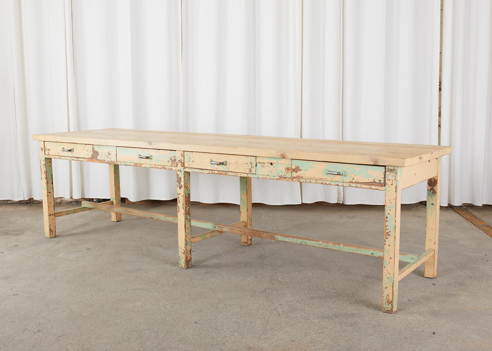 Monumental French industrial work table or farm potting table with four large storage drawers. The long table is crafted from pine and features a later added pine plank top nearly 2 inches thick. The trestle style base has six large square legs