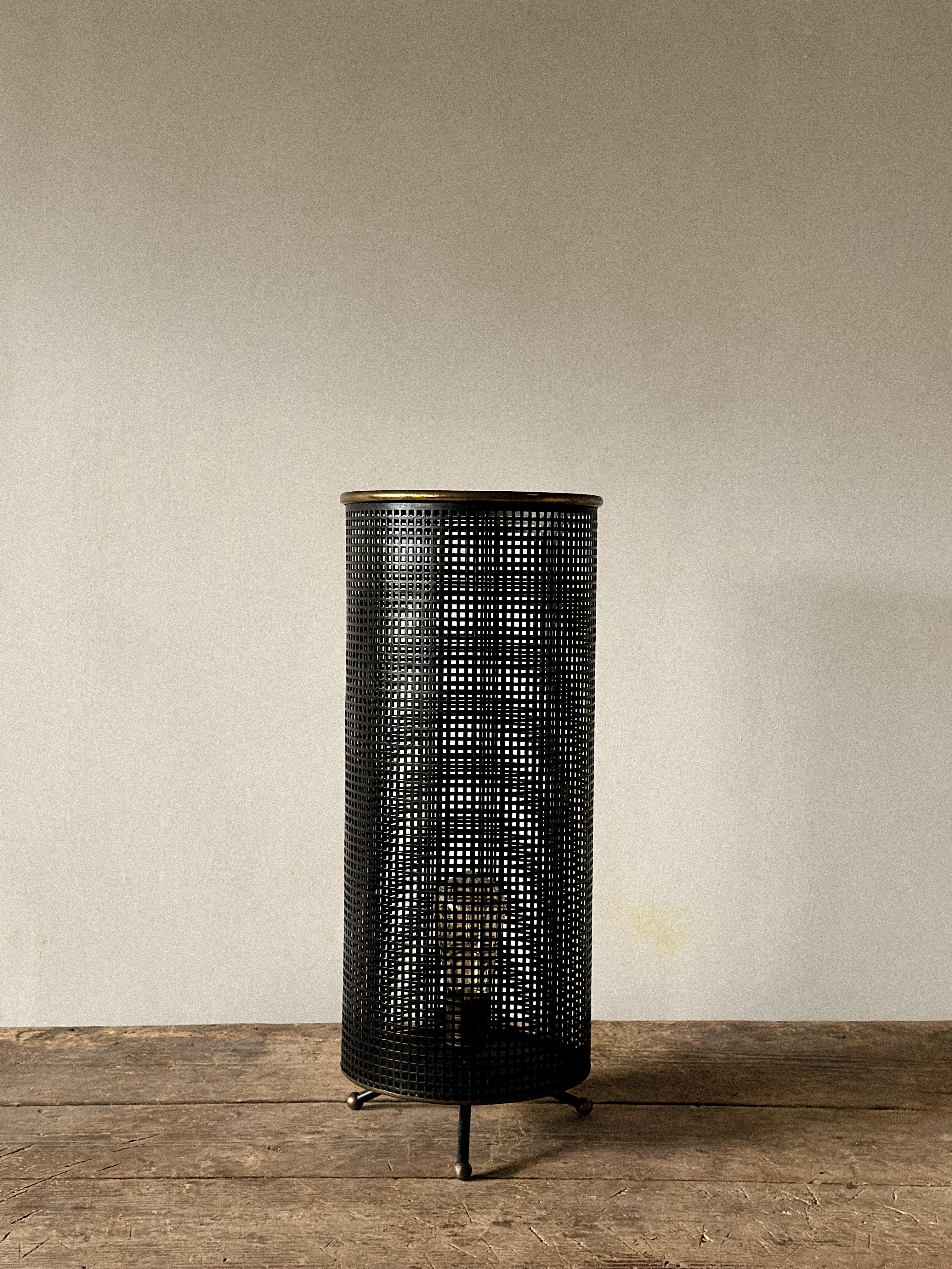 Lámpara de mesa industrial francesa, a la manera de Mathieu Matégot, Francia, hacia la década de 1950.

Pantalla de metal perforado lacado en negro sobre base trípode con detalle de borde de latón. Una pieza escultórica y atmosférica representativa