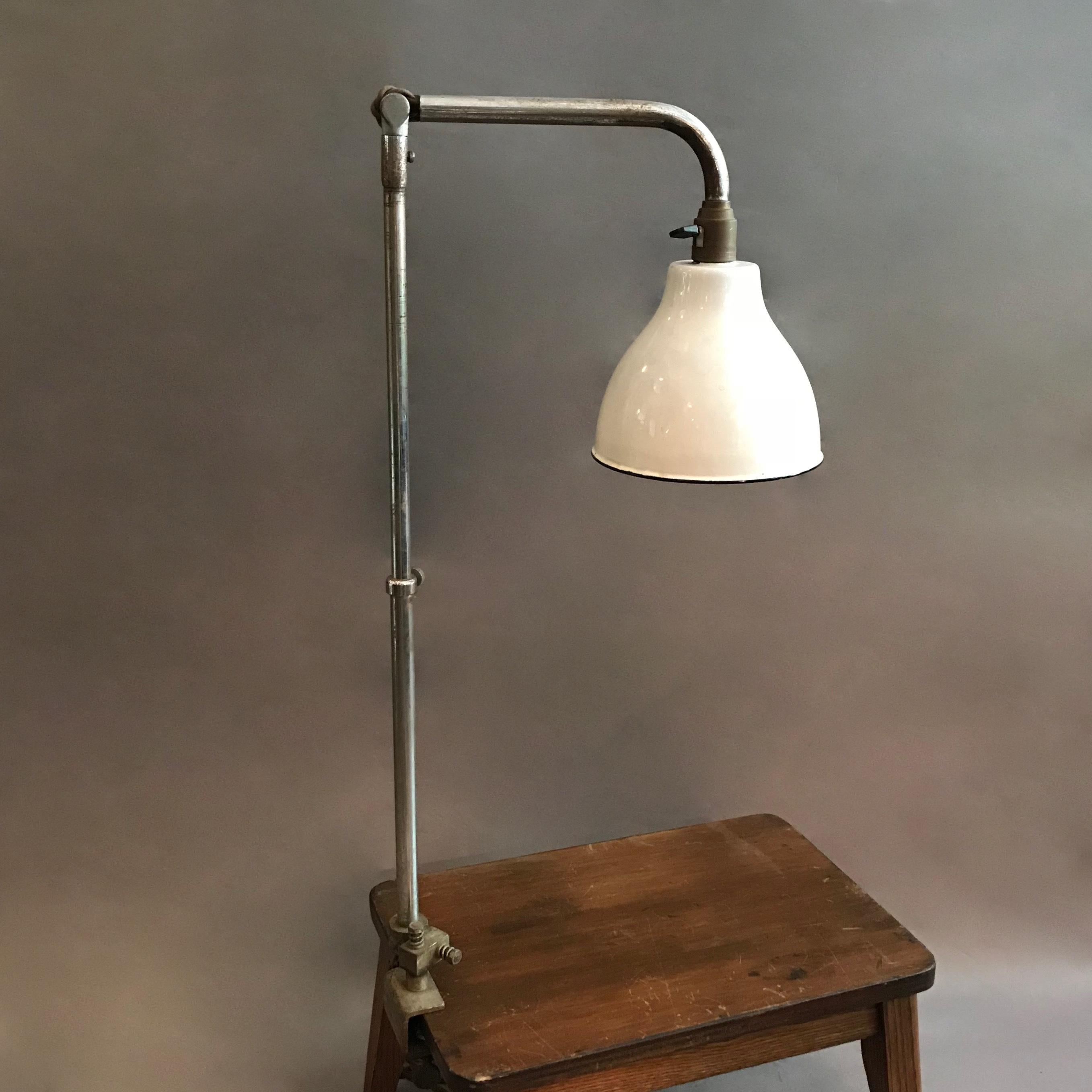 French, industrial task lamp by Alphonse Pinoit for Ki-E-Klair features a height adjustable, chrome-plated, telescopic stem with adjustable arm and white enamel shade. The lamp has a double screw clamp that attaches to a surface.