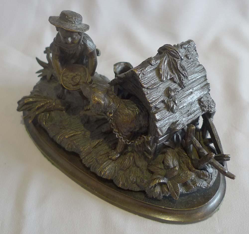 An attractive and unusual patinated bronze inkwell of a child feeding his dog which is chained to its kennel. The top of the kennel lifts off to reveal the porcelain inkwell within. The child in 19th century clothes of smock and hat and holding a
