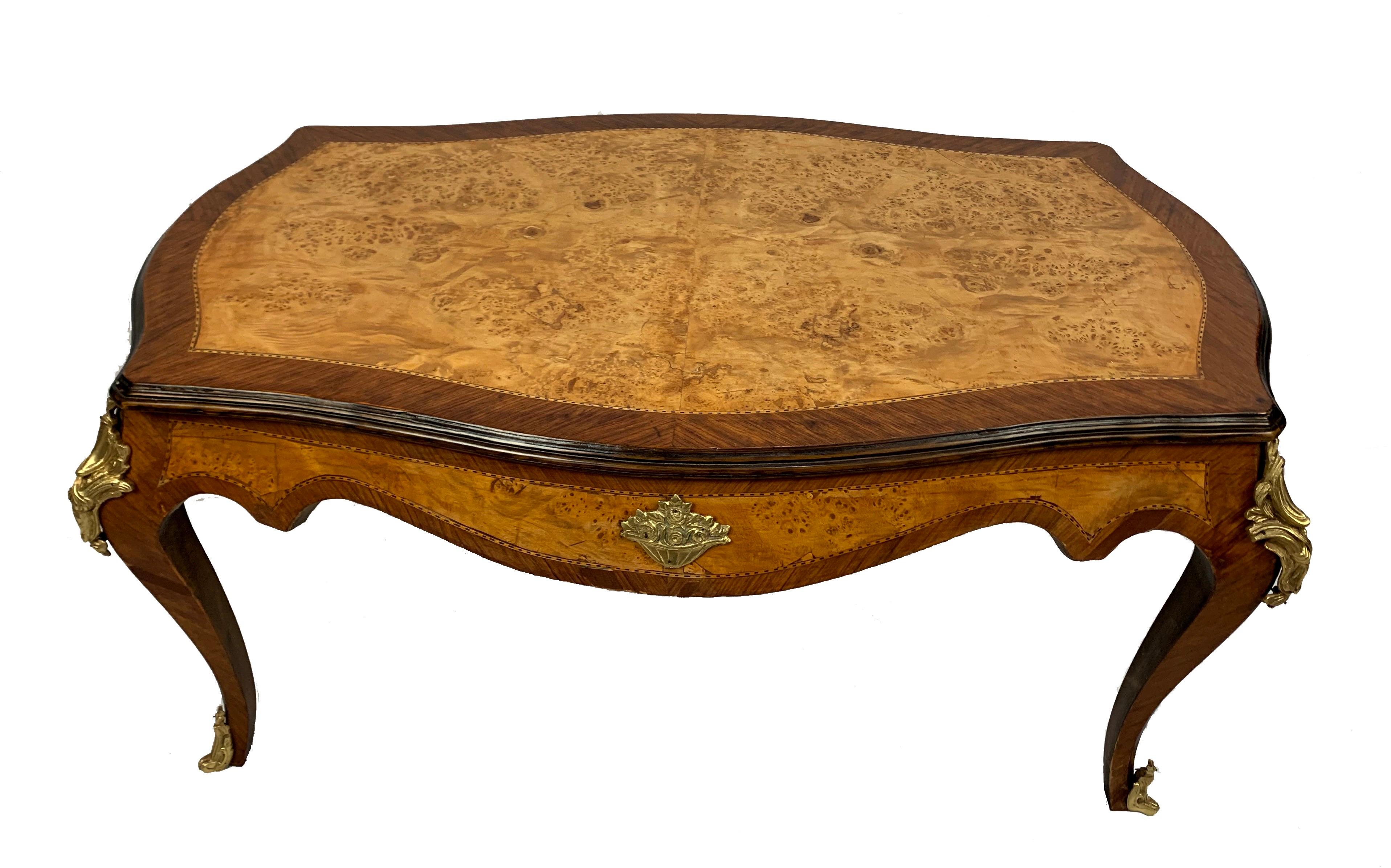 French coffee table features an exquisite rectangular burled walnut butterfly veneered top. Features gilt bronze decoration on the legs as well as on the front and back. With its exquisite burl walnut veneer top and elegant lines, this French coffee