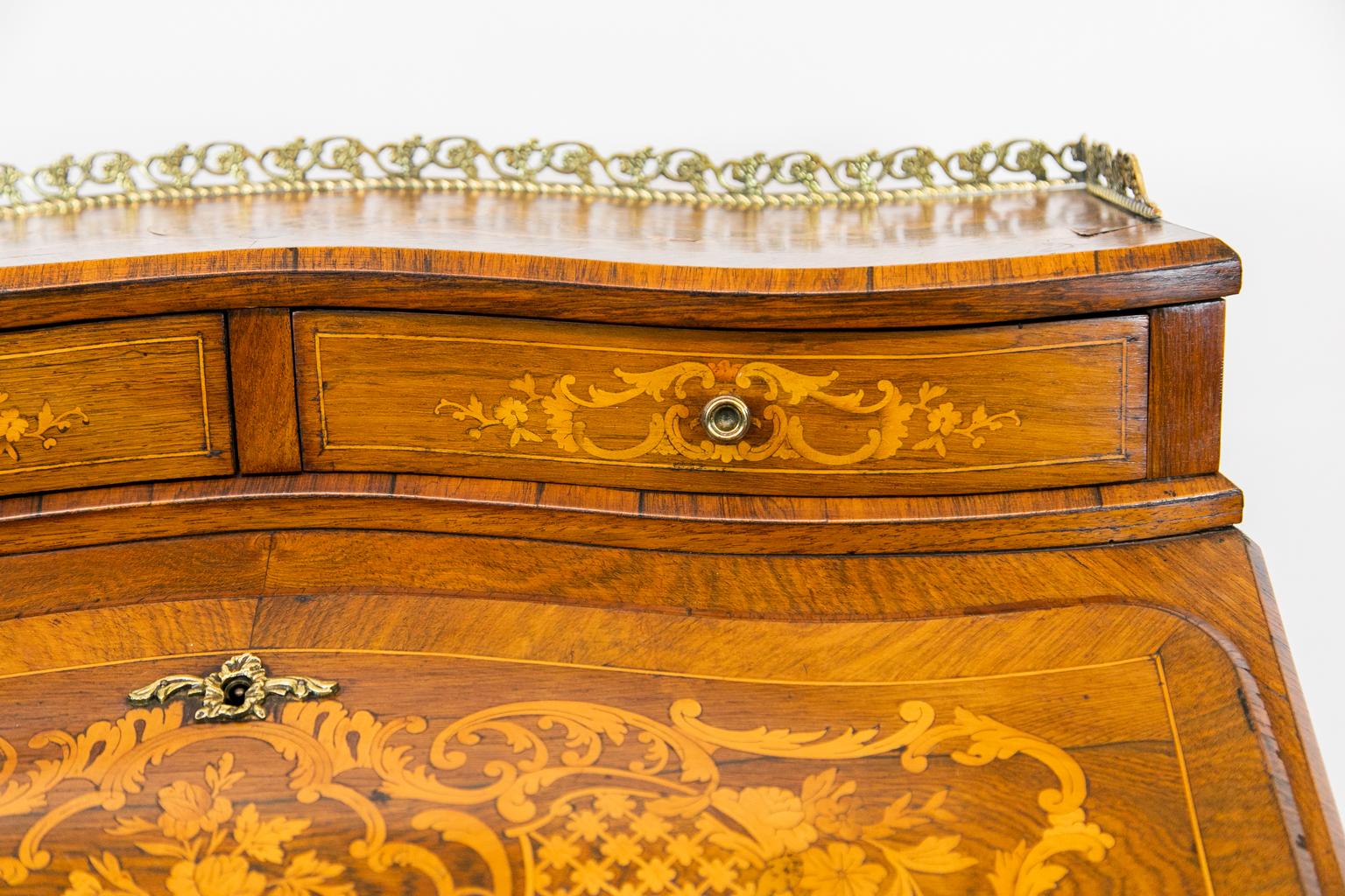 French inlaid ladies desk, with bombe shaped sides and have elaborate satinwood and boxwood inlays with floral and arabesque designs as well as inlaid diapered cartouches. The three sides have book matched rosewood cross banding. The interior has