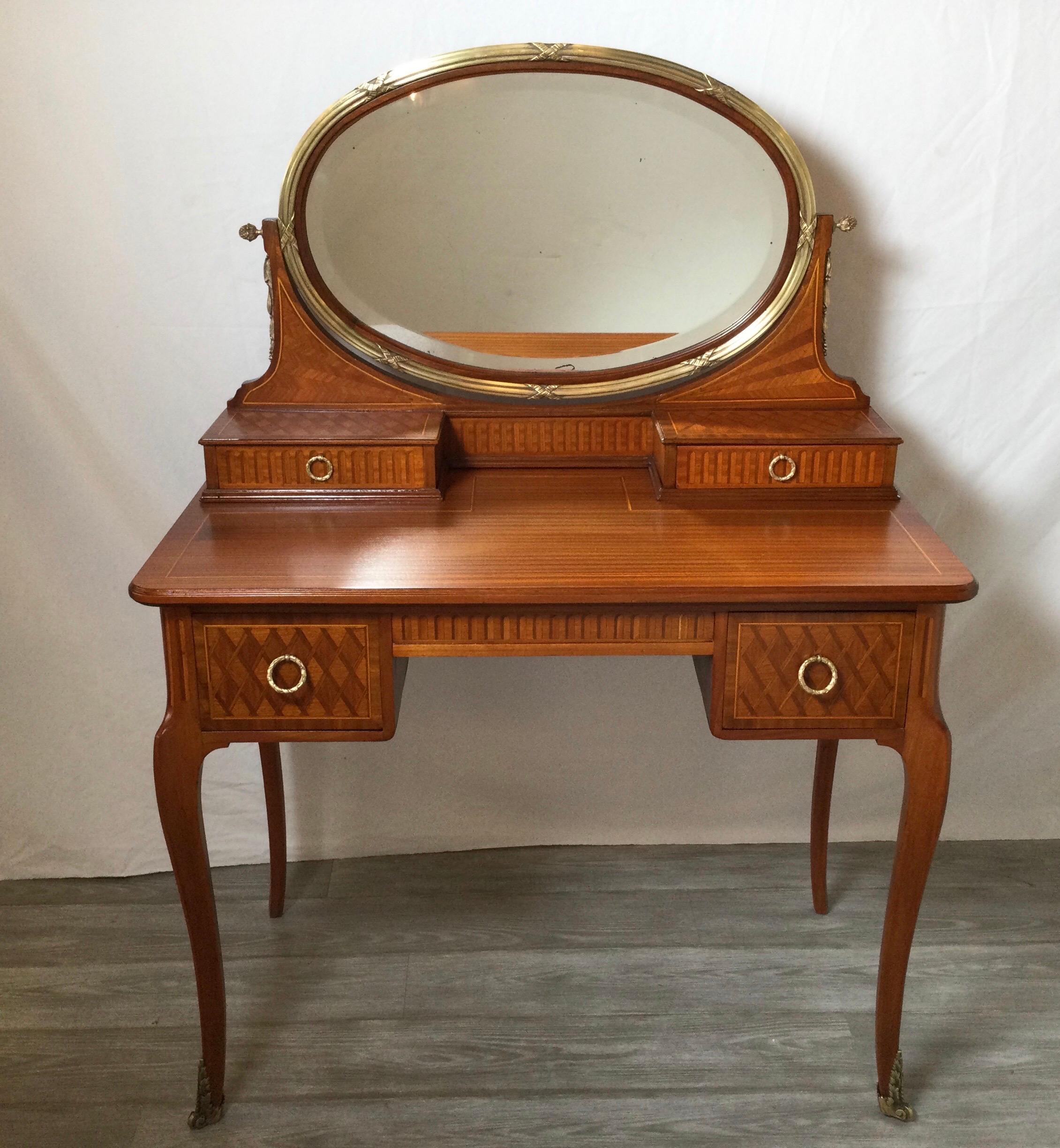 The vanity with oval bronze mount surrounding the beveled mirror with one small drawer on each side above the larger drawers resting on curved cabriole legs. The inlay in a detailed basket weave on the drawers fronts with all-over inlay on the other