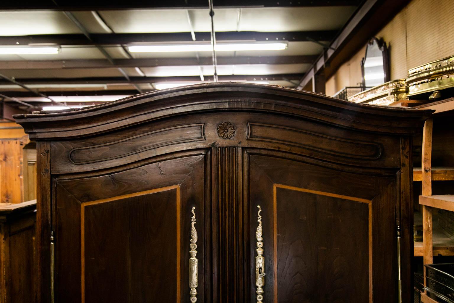 The frieze of the armoire has serpentine carved panels. The doors are inlaid with satinwood. The center panel has three carved shaped moldings. The lower apron has a carved stylized scallop shell in the center. The interior is open but has three