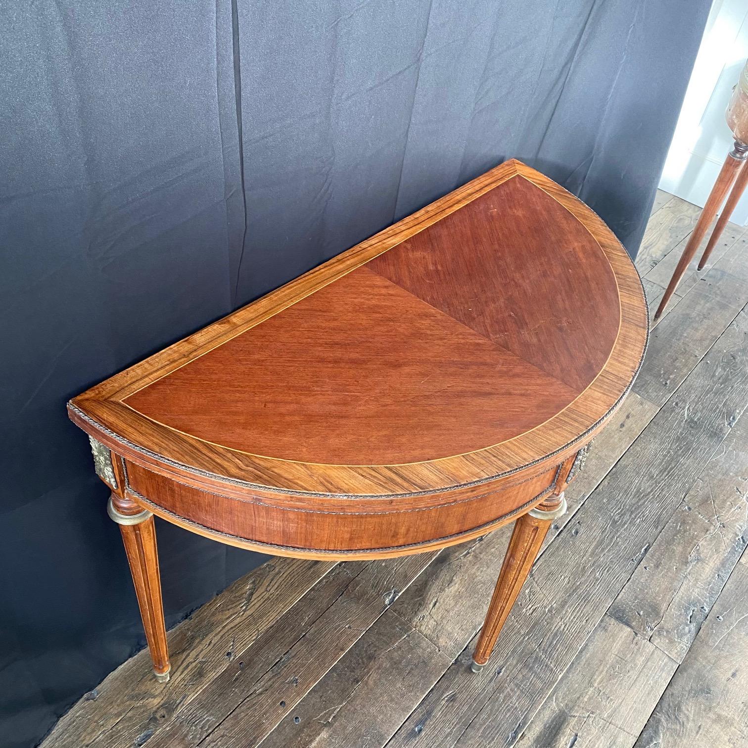 French game table and console. When closed it is a demilune console inlaid in walnut and fruitwood. When open the circular surface is embossed leather and wooden inlaid stripe border (see photos) to make a game table.  Console supported by solid