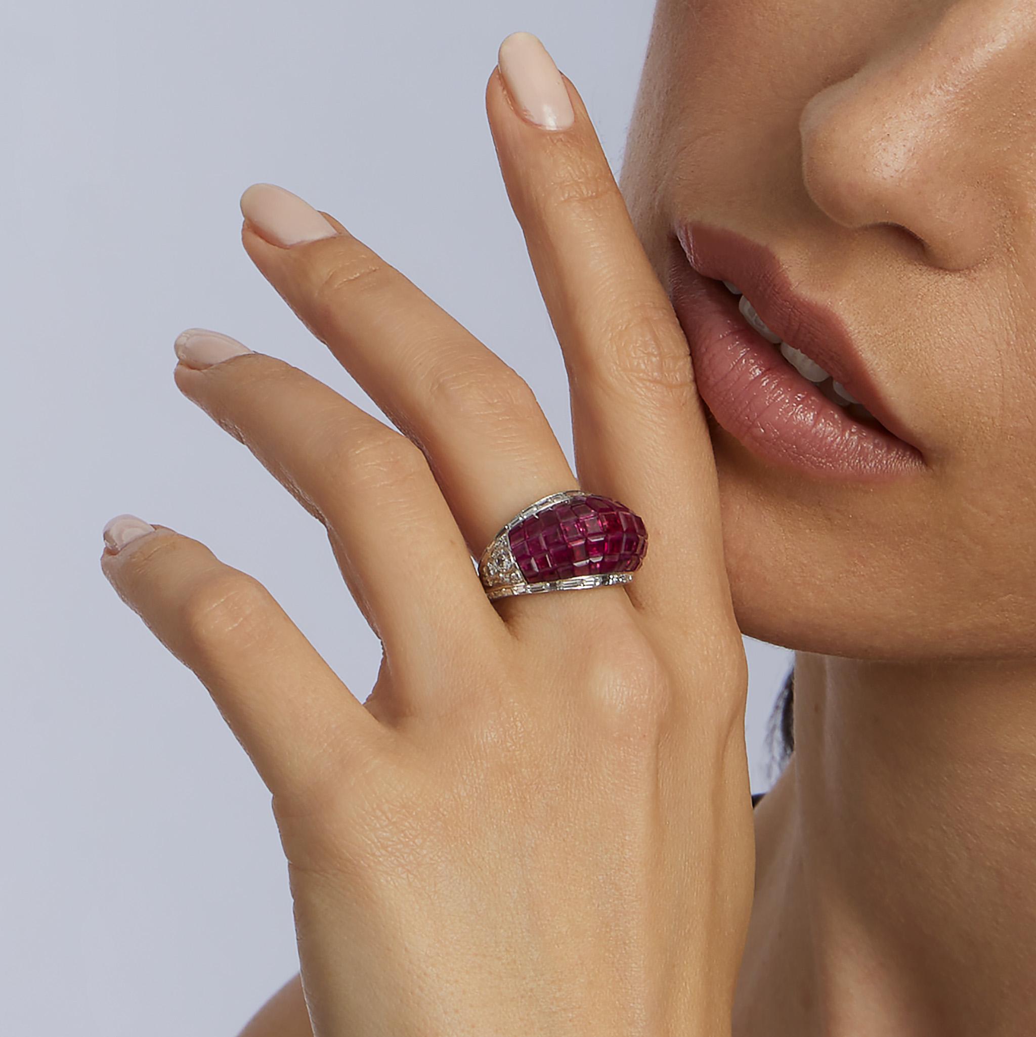 Dieser Bombé-Ring, der um 1980 in Paris hergestellt wurde, ist mit Rubinen und Diamanten besetzt. Die voluminöse, gewölbte Form ist unsichtbar mit Rubinen im Kalibré-Schliff besetzt, die mit Diamantbaguetten eingefasst sind. Die Schultern sind mit
