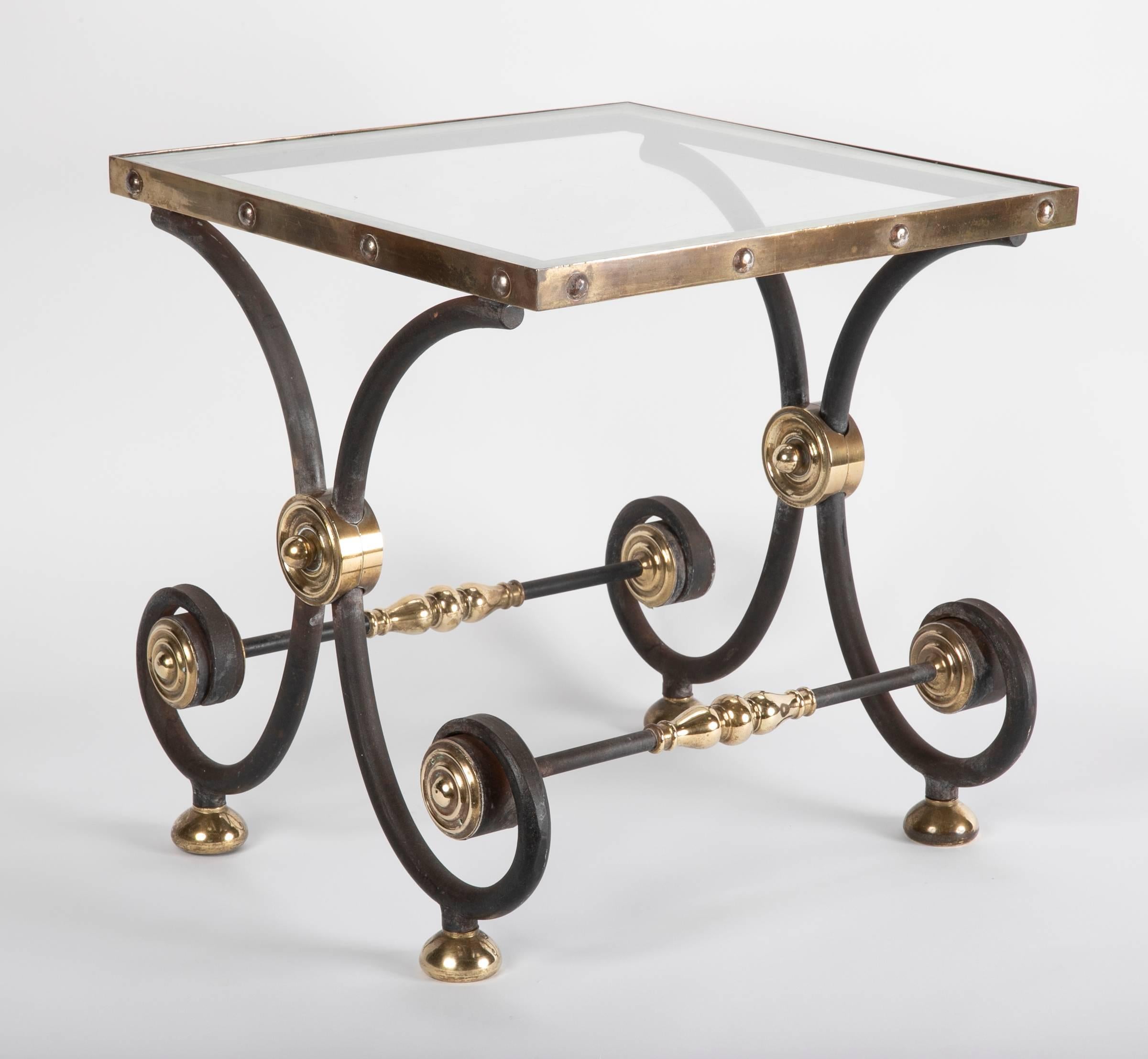 An Art Nouveau period French wrought iron and brass side or cocktail table with glass top. If you are looking for a unique side table this is it. With its elegant profile of wrought iron scrolls joined by finely turned brass bosses, the glass top in