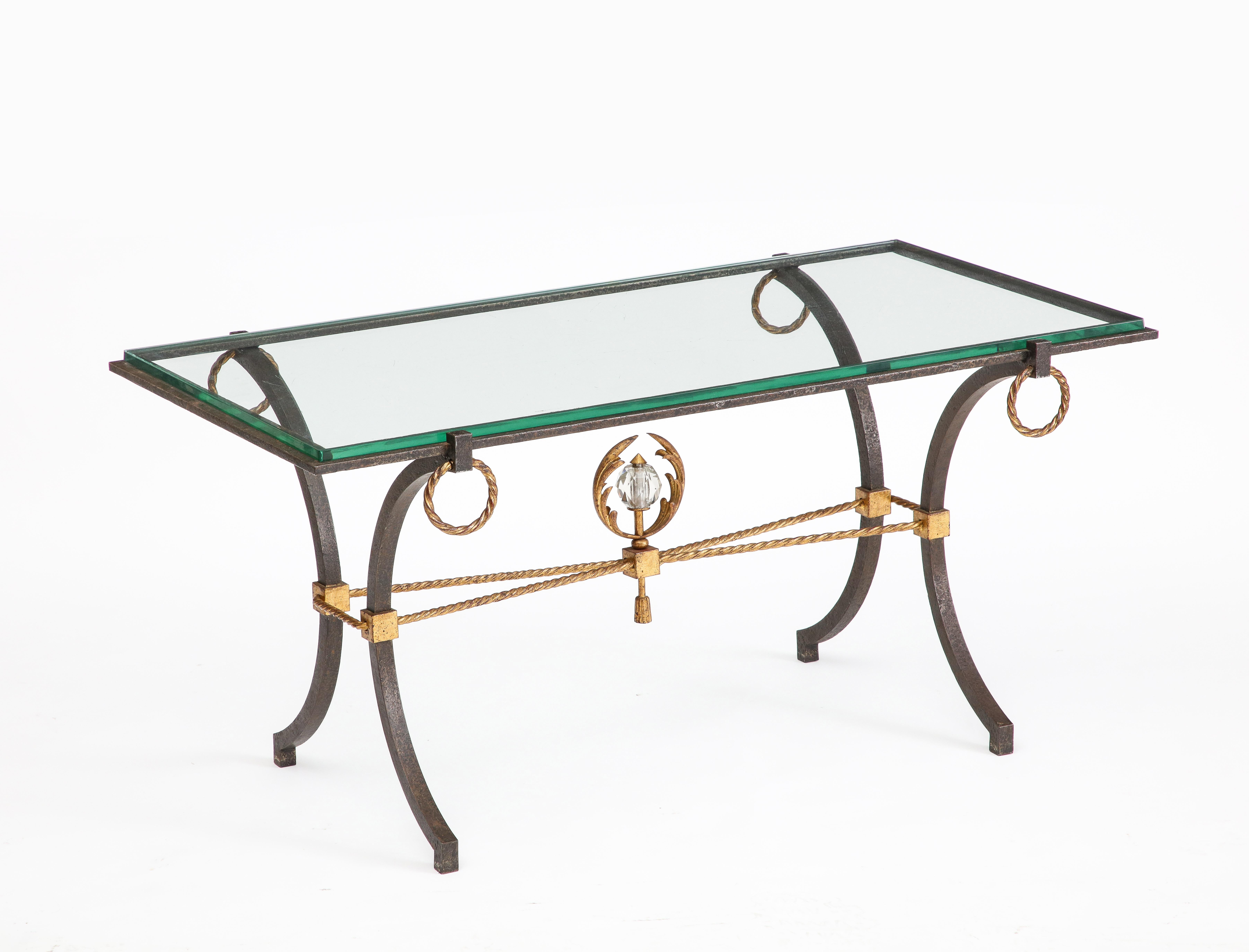 French iron and gilt coffee table, in the style of Poillerat, c. 1940. The curved iron legs support the glass top through which you can view an ornamental gilded centerpiece supported by gilded bronze rope stretchers. The gilded rope motif is also