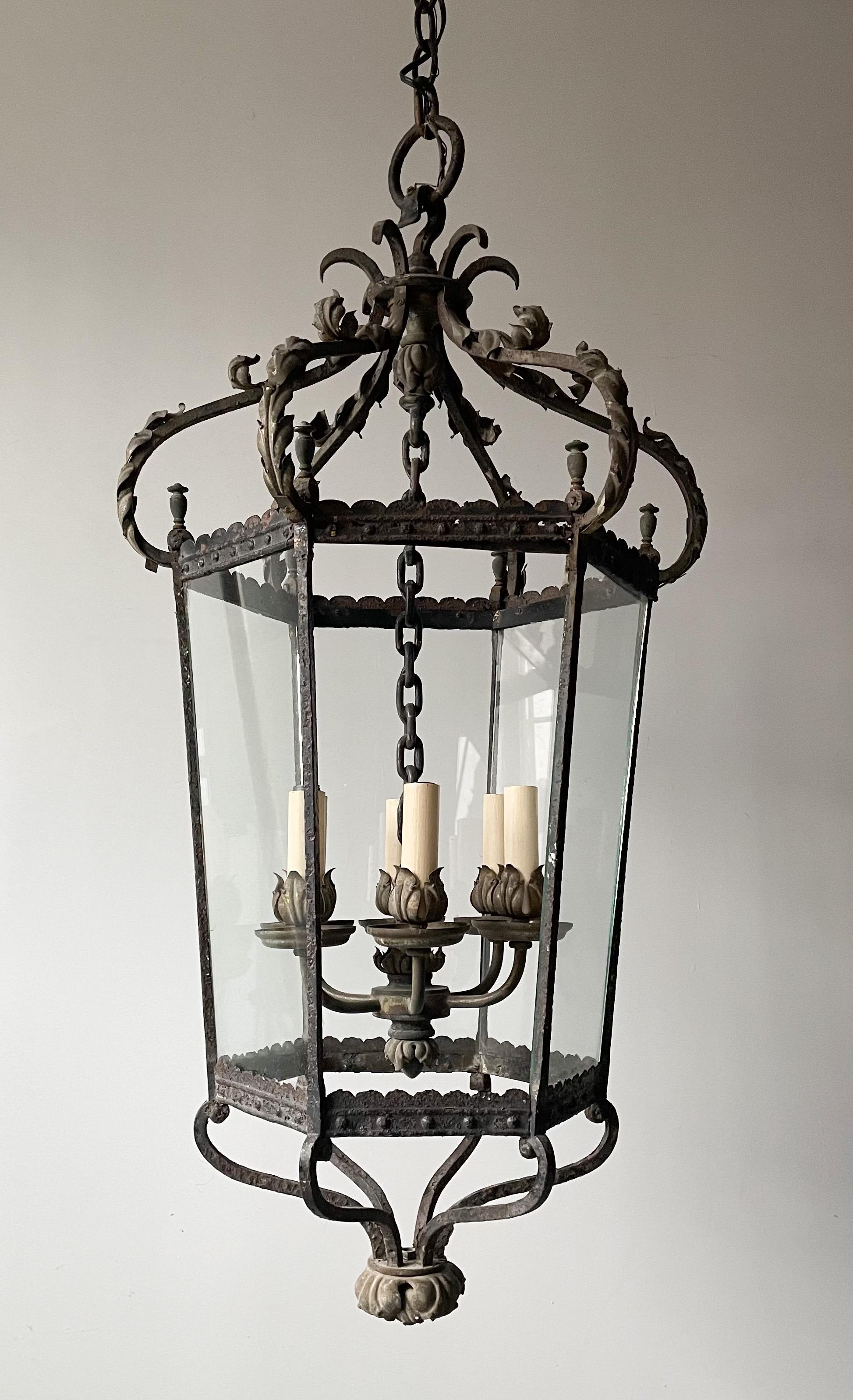 Beautiful, French 1940s iron and glass lantern in the Louis XV style.

The lantern consists of an iron frame with natural aged patina, it is decorated with acanthus leaves and filagree details. Six glass panels house 4 candelabra sockets. 

The