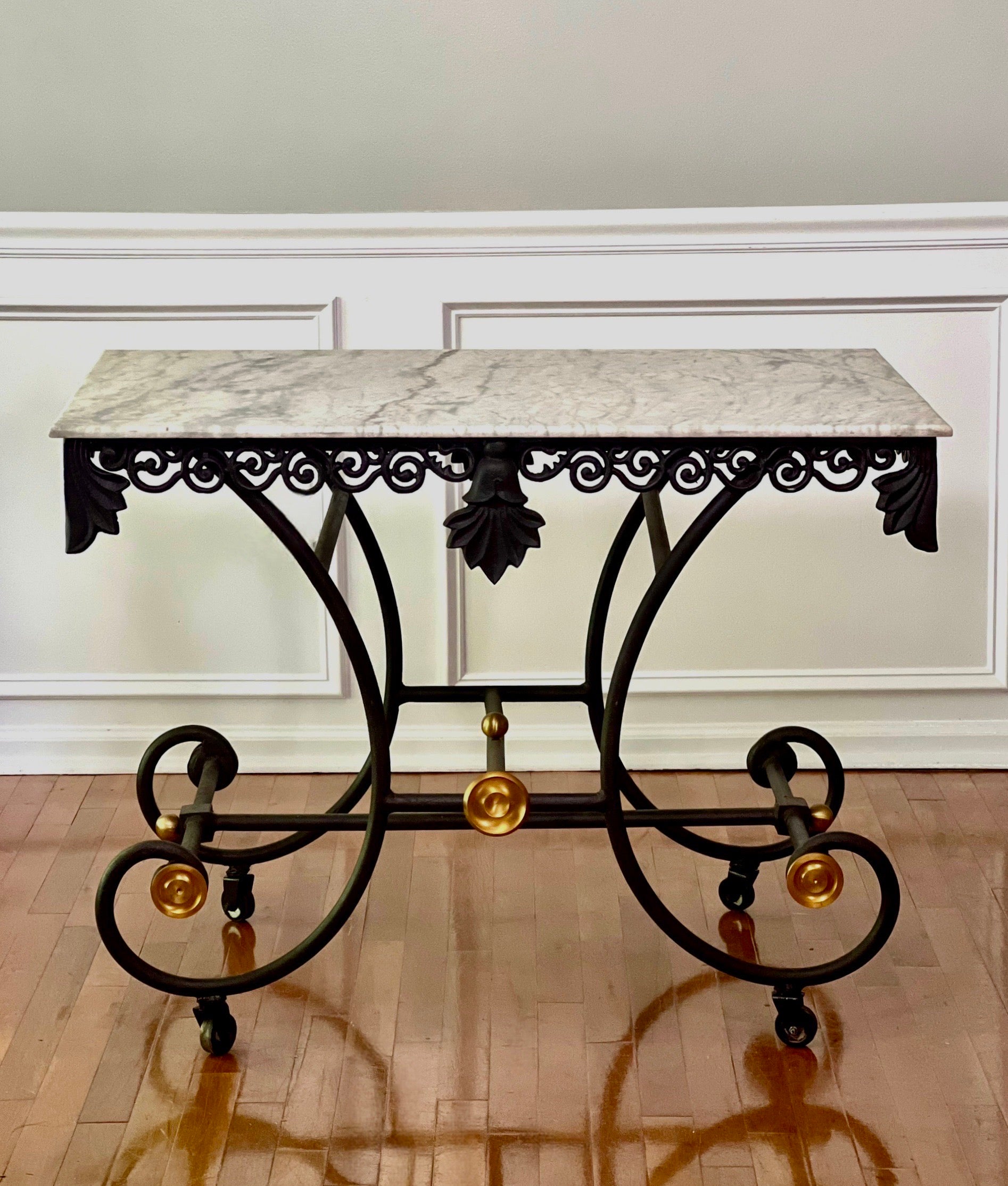 A gorgeous, classically styled French iron pastry table with a Carrera marble top on original casters, mid 20th century.

It features a beautifully curved wrought iron base with brilliant gilt medallions and ball finials and an ornate cast iron