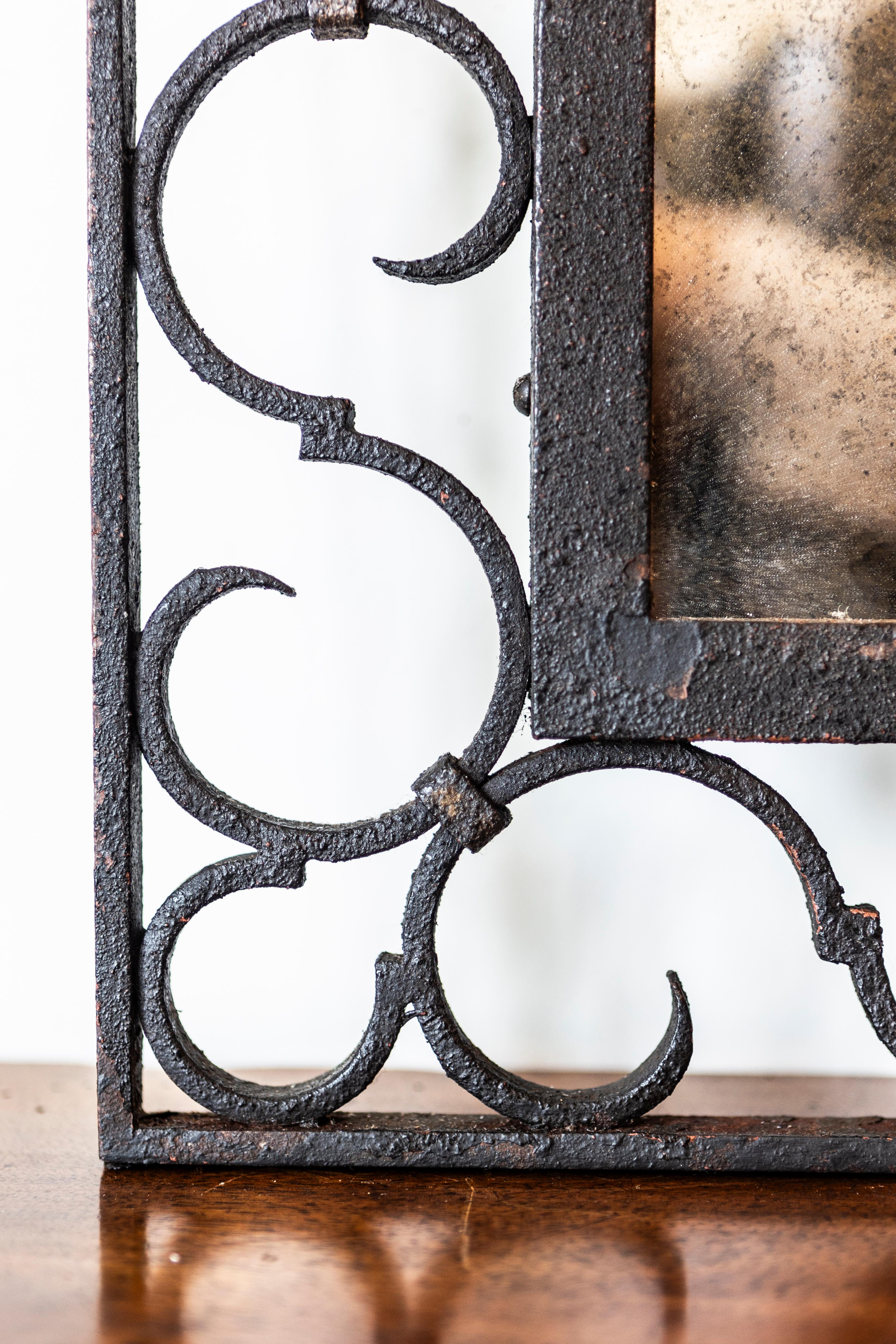 Miroir en fer français du XXe siècle, à la silhouette arquée et aux motifs de volutes. Ce miroir en fer français du XXe siècle dégage un charme particulier avec sa silhouette voûtée et ses motifs en volute. Le cadre ajouré a été réalisé de main de