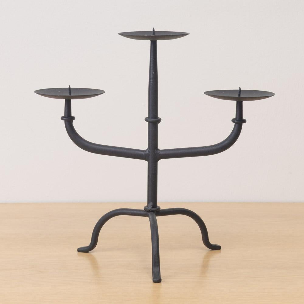 Candelabro a tre bracci in ferro vintage proveniente dalla Francia. Bracci sottili e curvi su una base di ferro a tre gambe. La finitura originale mostra una buona età e patina. 