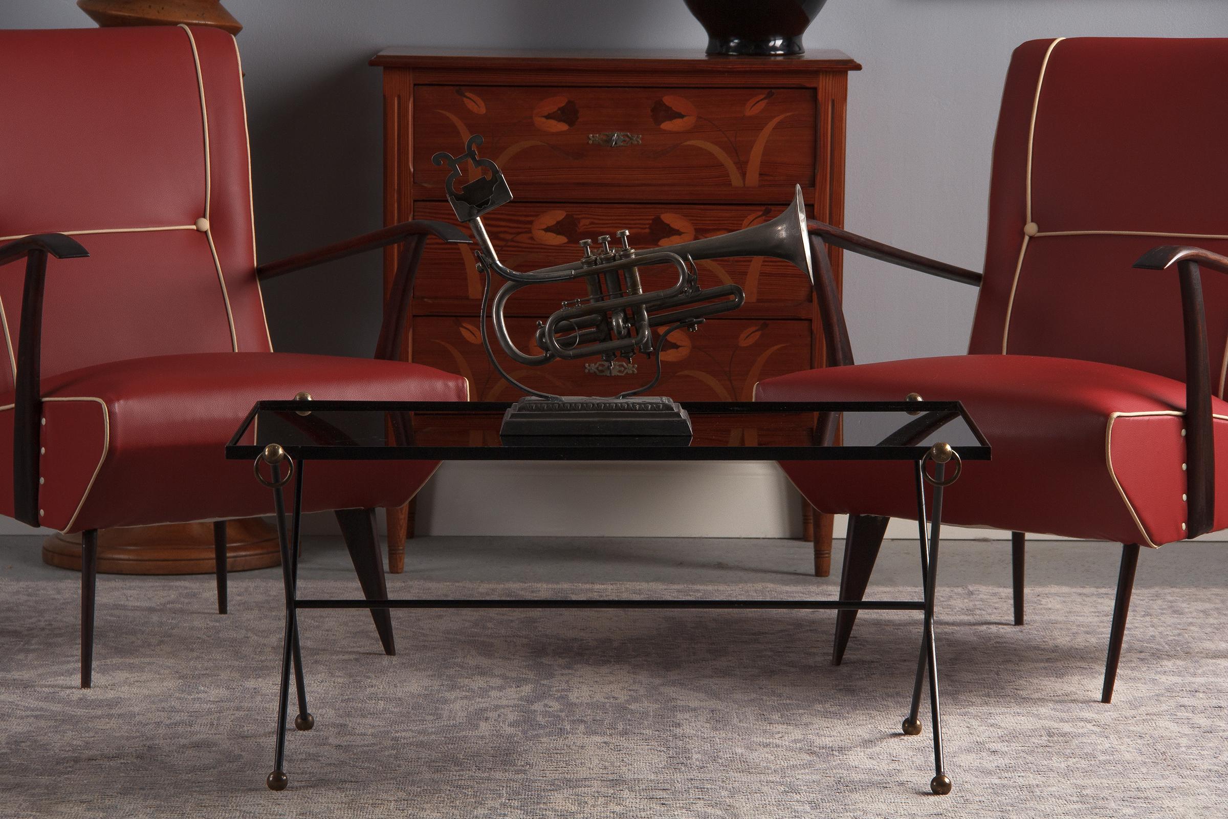 A swanky painted iron and opaque black glass coffee table attributed to Jaques Adnet, circa 1950s. Black iron bars bent into X-form legs are punctuated at top and bottom by brass balls, swinging brass loops pierce the upper balls. A single black bar