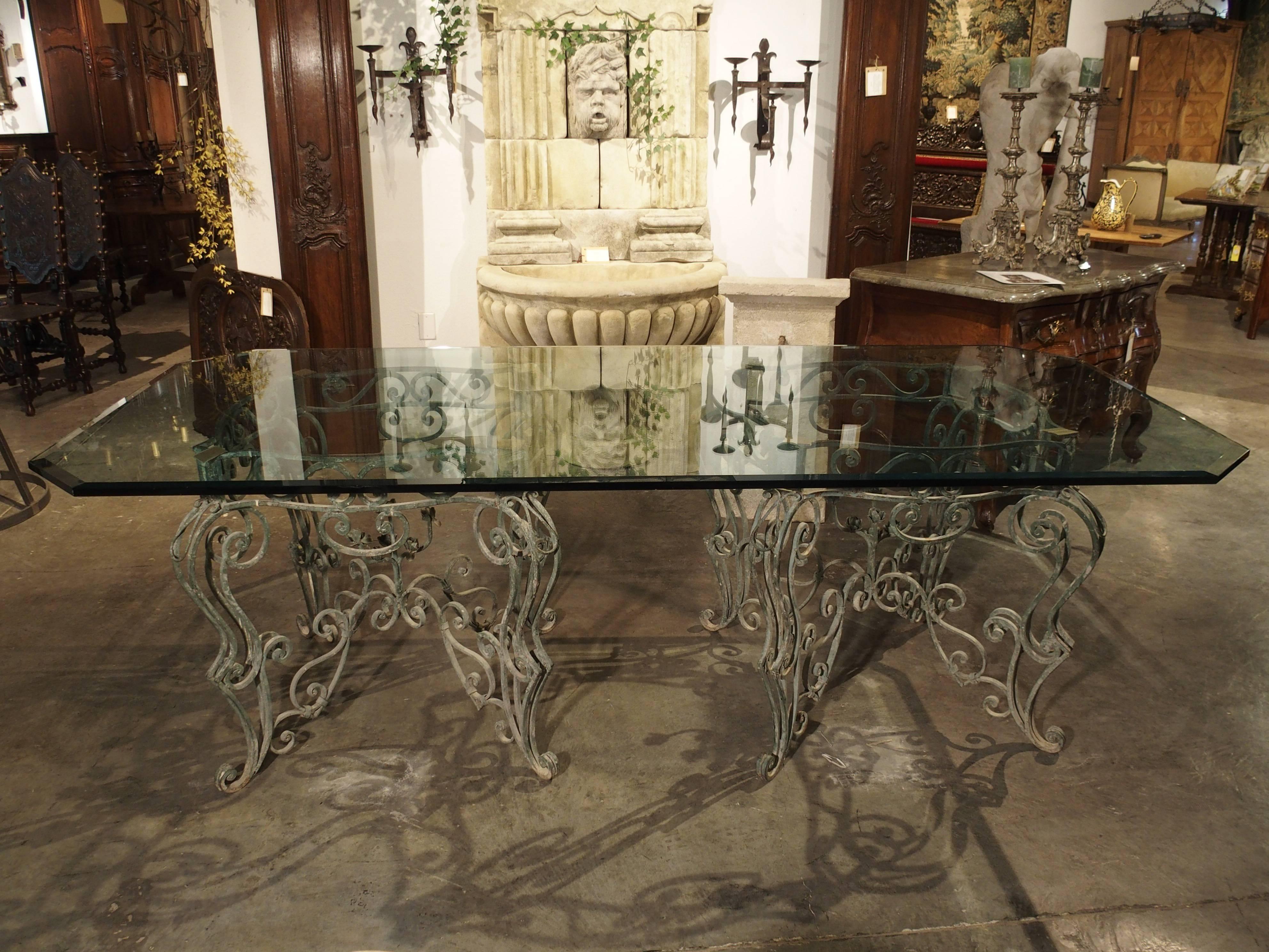 This glass topped table from France is supported by two patinated Verdigris iron bases. The bases are square with an abundance of open worked C and S scrolls. At the centre of each base, there are iron bouquets of seven roses each. On the apron are
