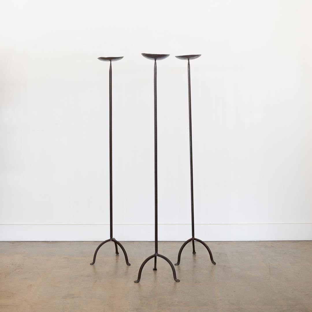Unique set of 3 wrought iron floor candle stands from France, 1950's. Circular drip pan sits on a slender stem and forged iron tripod base. Beautiful addition to any room. Sold as a set of 3. 
Measures 48.25