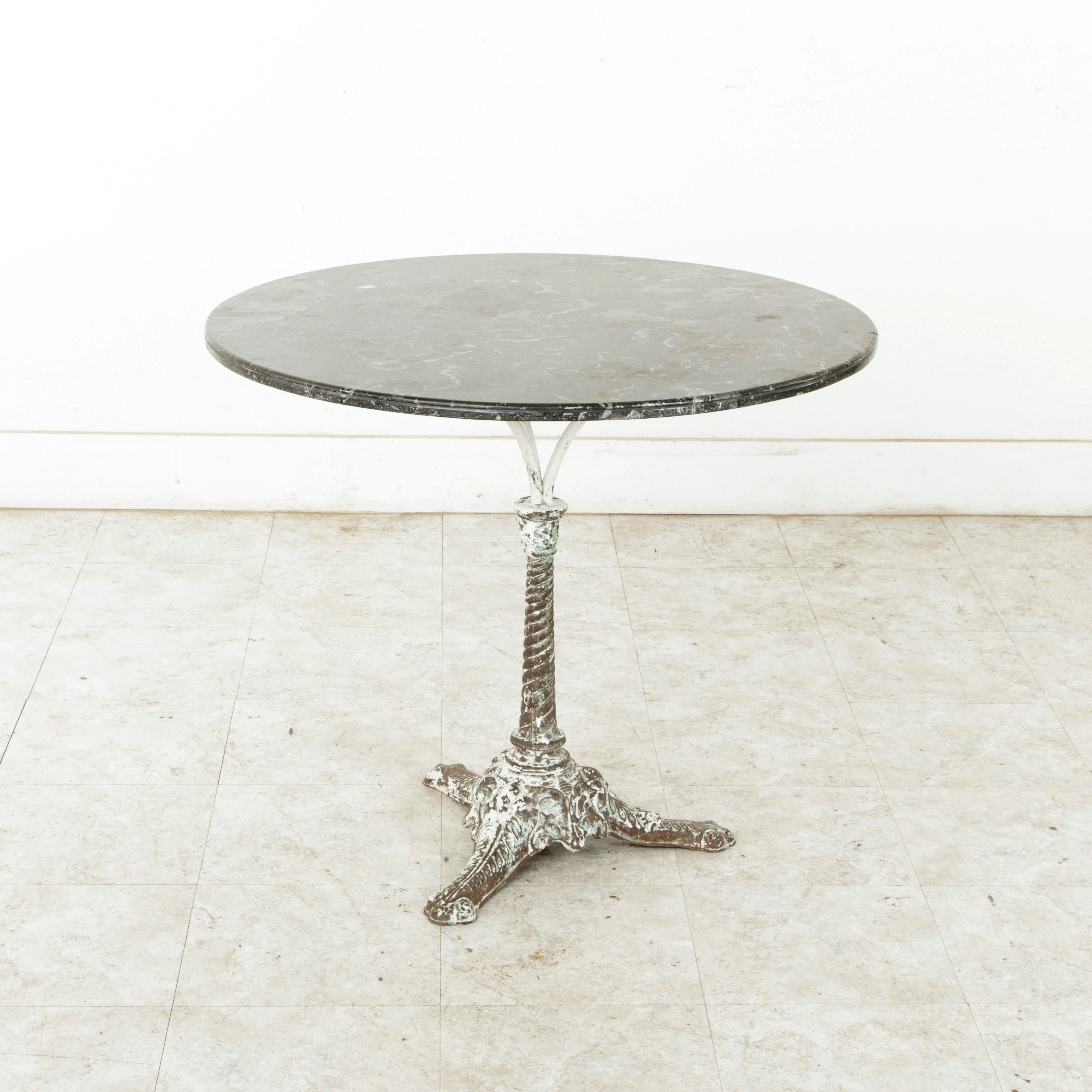 This French iron garden table from the turn of the 20th century features a 32-inch diameter Saint Anne black marble top with white and grey veining. The marble top rests on a iron tripod support joined to the central spiraling pillar. The pillar