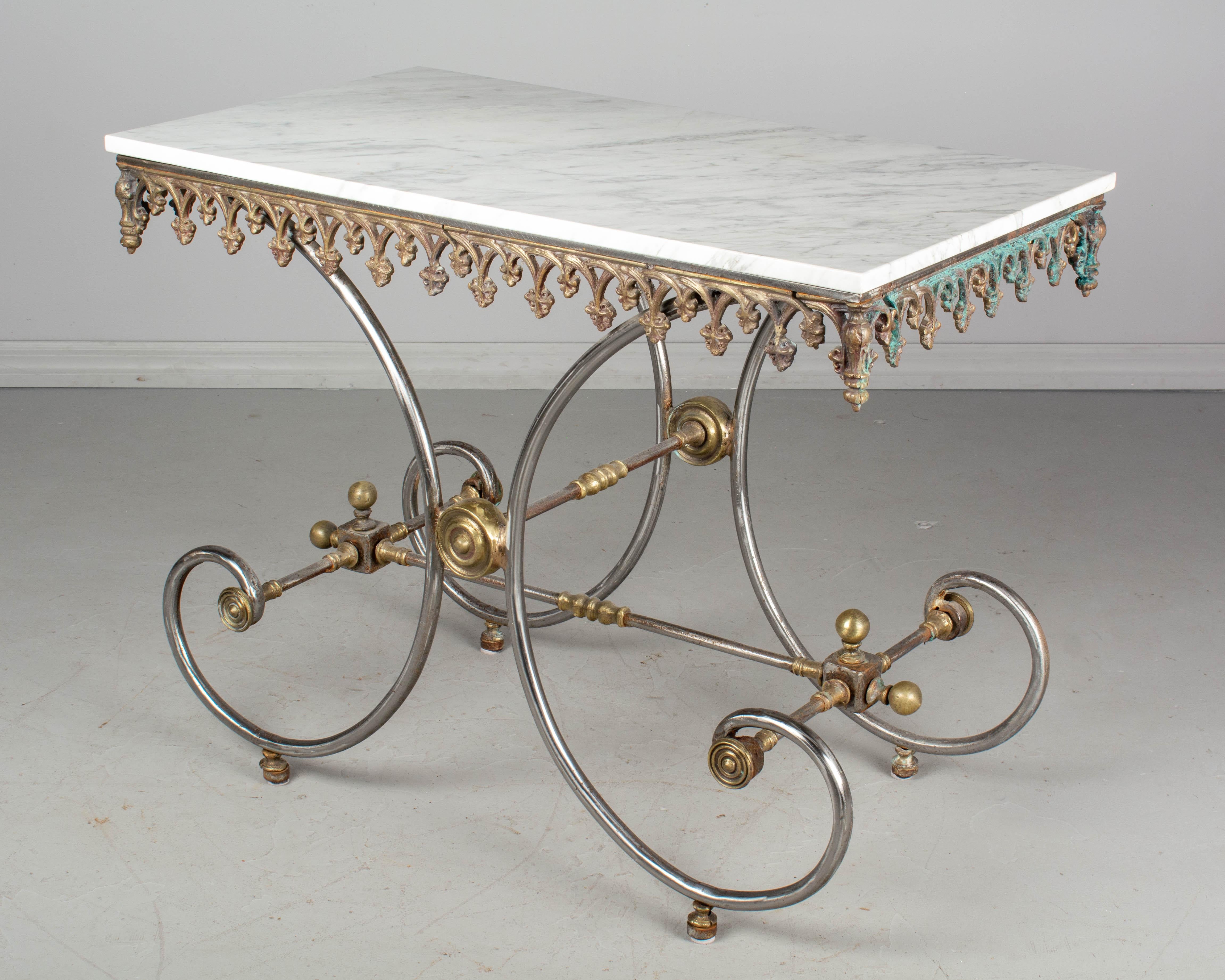 A French pastry table polished curved wrought iron base and brass hardware. Decorative cast iron frieze around the perimeter. White veined marble top. Condition of metal is as found, with rust and blue green patina on one side. A good replica of a
