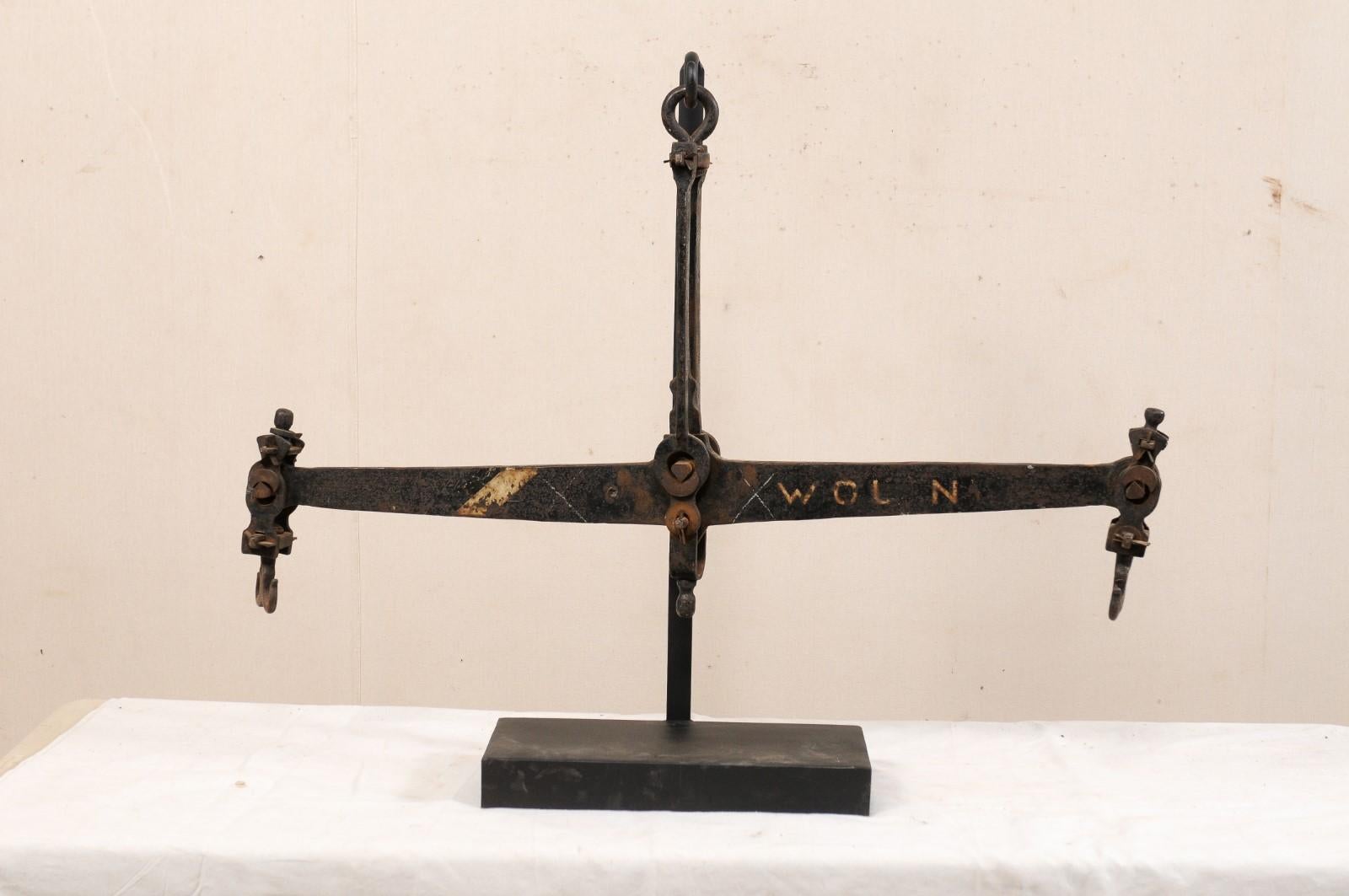 A French iron scale from the mid-20th century presented on custom iron stand. This vintage scale from France is a sizable piece, being over 3.5 feet in length, and features an elongated central bar, with double-hooked ends, and connecting to top at