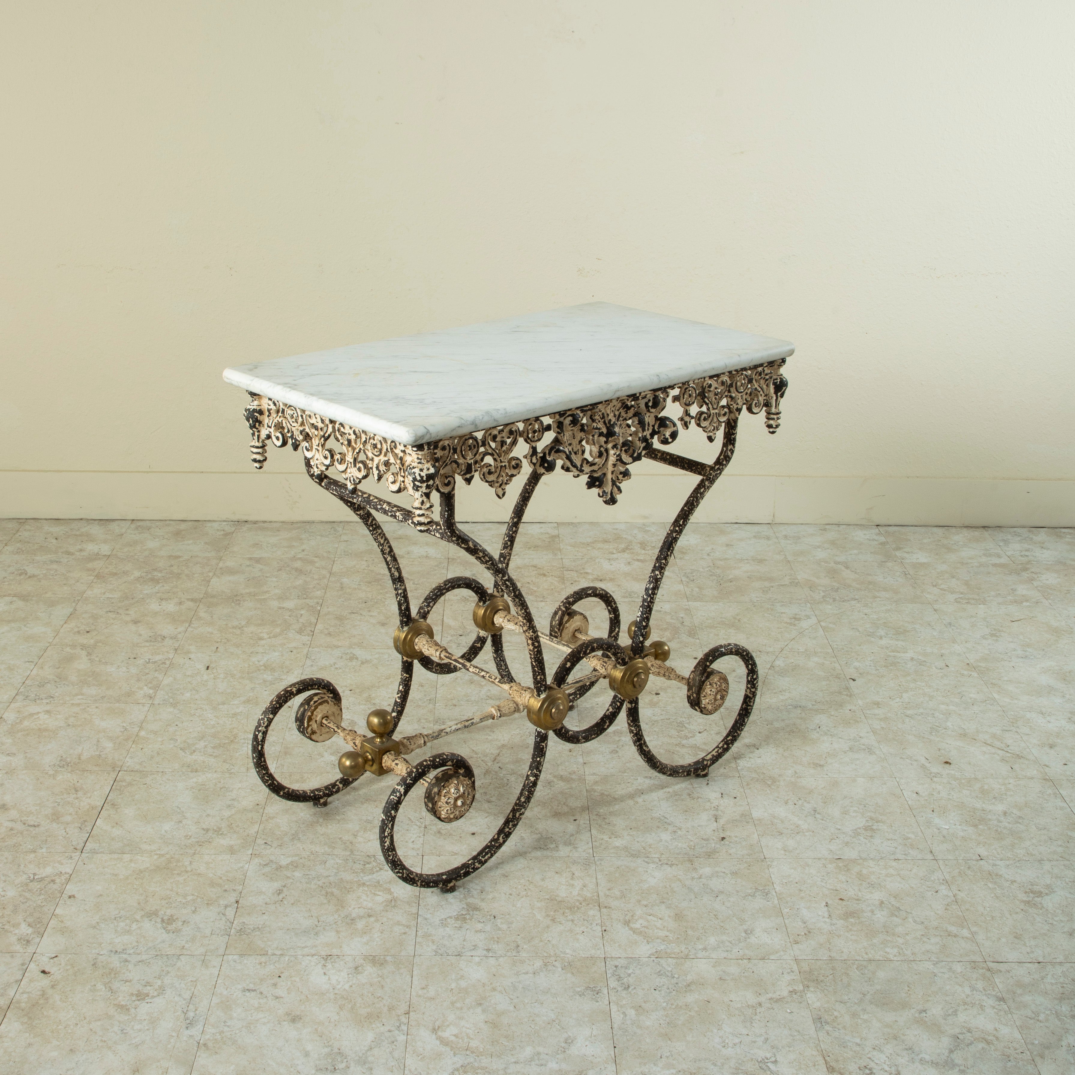 This mid-twentieth century French cast iron pastry table features a solid white marble top. The marble rests on an intricately scrolled iron base detailed with bronze medallions that connect the legs. Vestiges of paint on the iron base lend a lovely