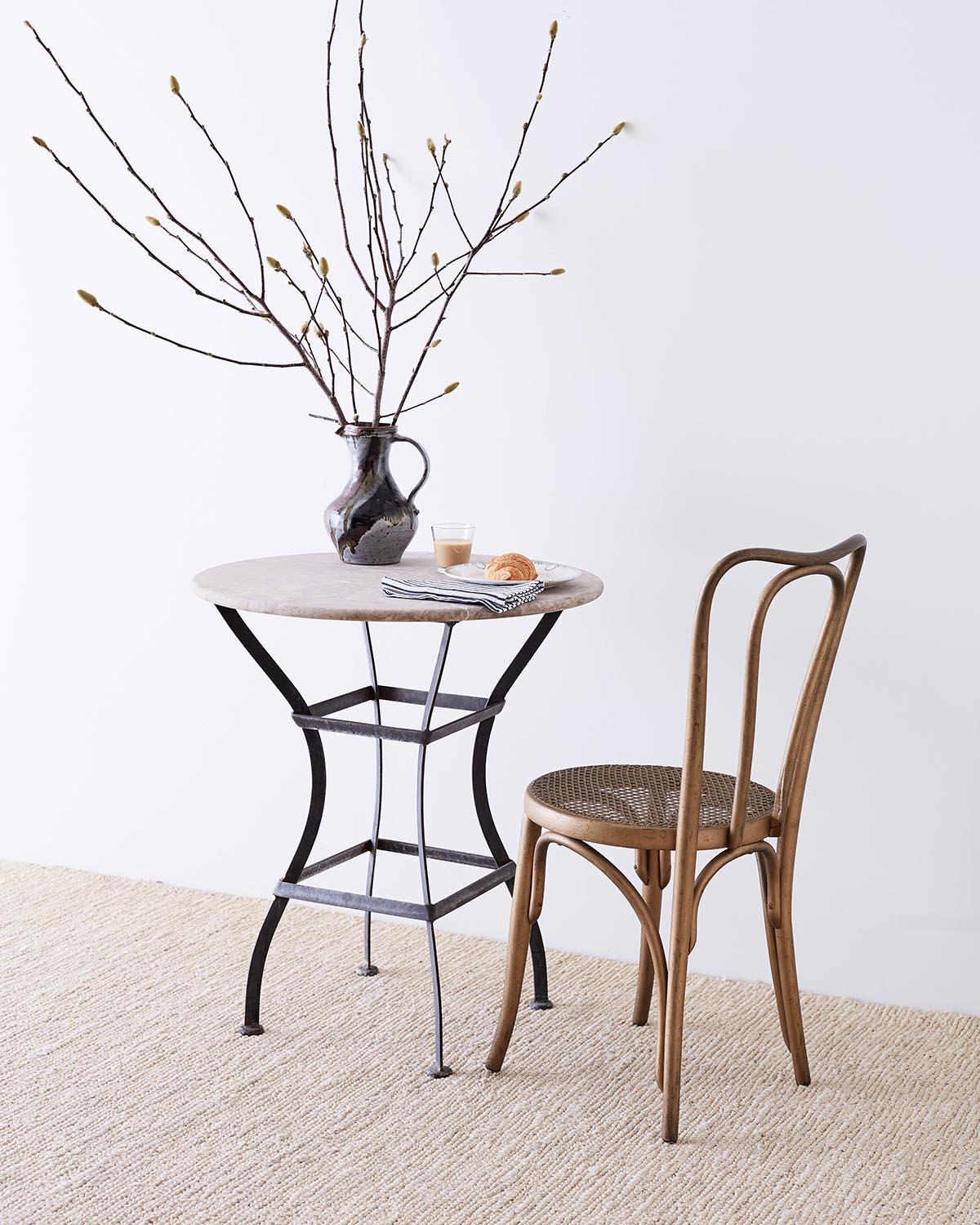 Sculptural French bistro table or cafe table featuring an iron base topped with a later molded stone top. The base is constructed from iron with an hourglass shape conjoined with square stretchers. The round top resembles limestone with natural