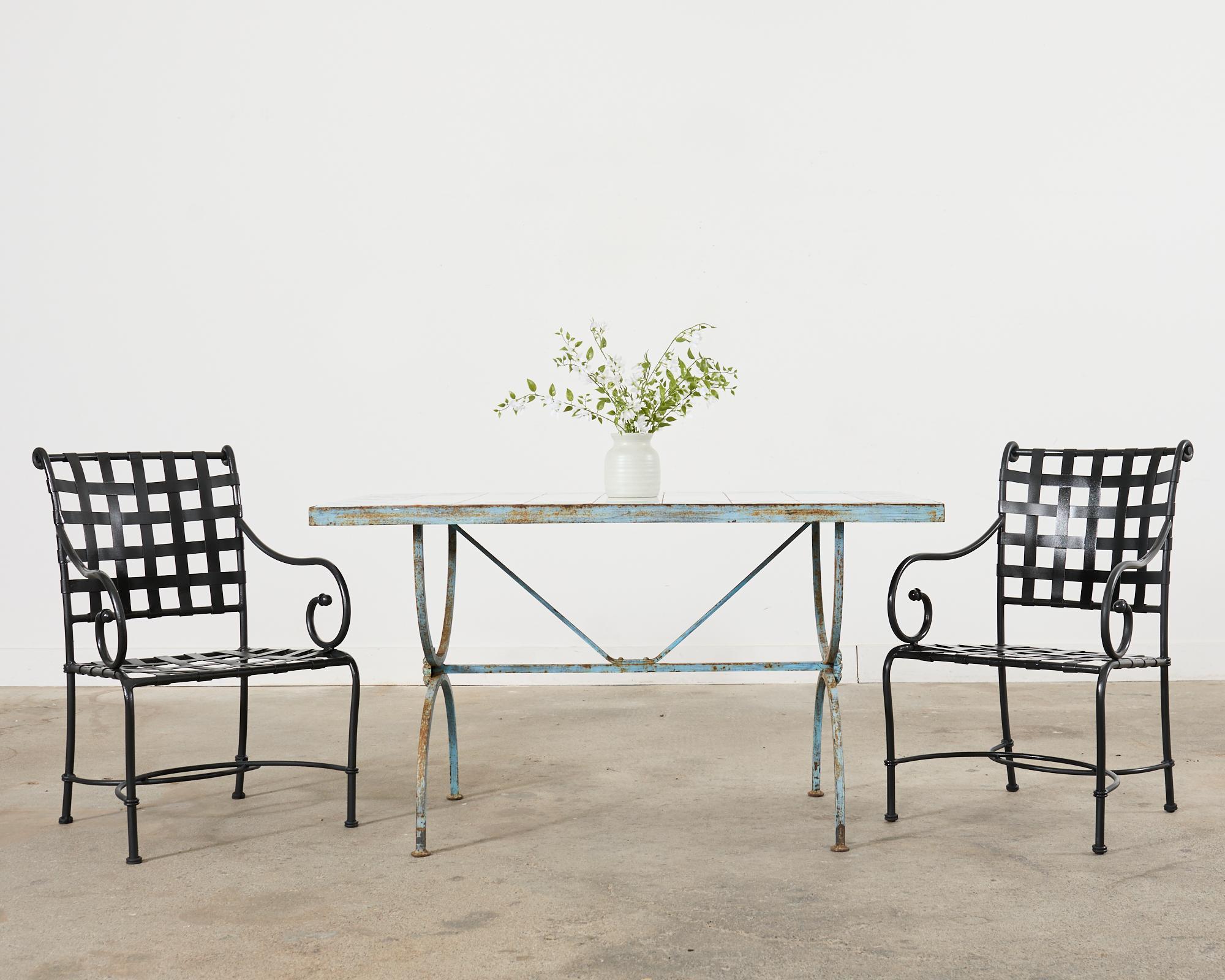 Charmante table de patio et de jardin à pied curule en fer français, avec un plateau en carreaux de céramique. Le plateau en carreaux blancs est bordé de motifs colorés de feuilles de vigne vertes. Le plateau est soutenu par un tréteau Curule de