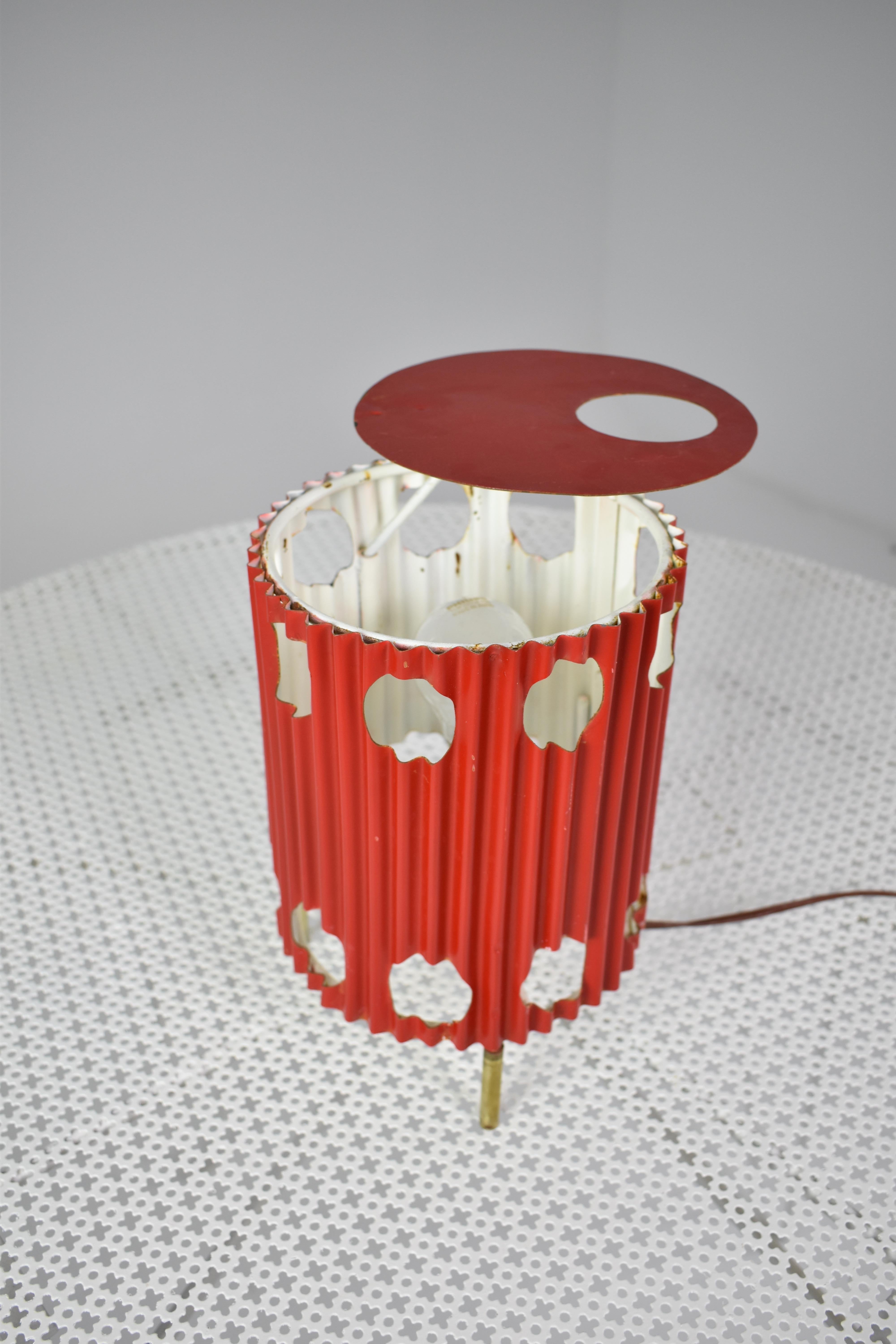 The highly collectible red 'Java' lamp, circa 1953, embodies Mathieu Matégot's artistic innovation, featuring pleated and perforated painted sheeted metal atop elegant brass tripod legs. Like a work of art, its striking design plays with light and