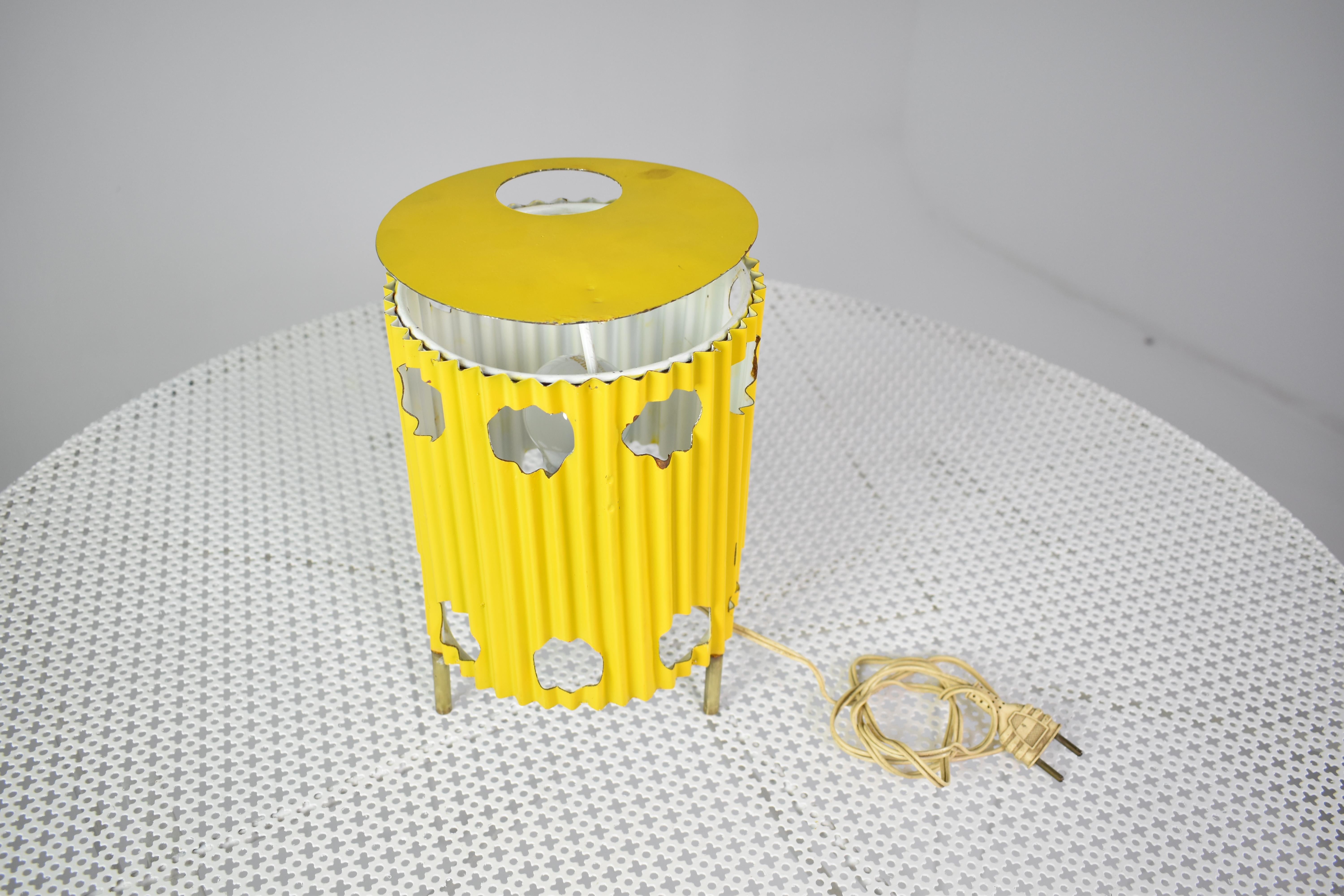 The highly collectible yellow 'Java' lamp, circa 1953, embodies Mathieu Matégot's artistic innovation, featuring pleated and perforated painted sheeted metal atop elegant brass tripod legs. Like a work of art, its striking design plays with light