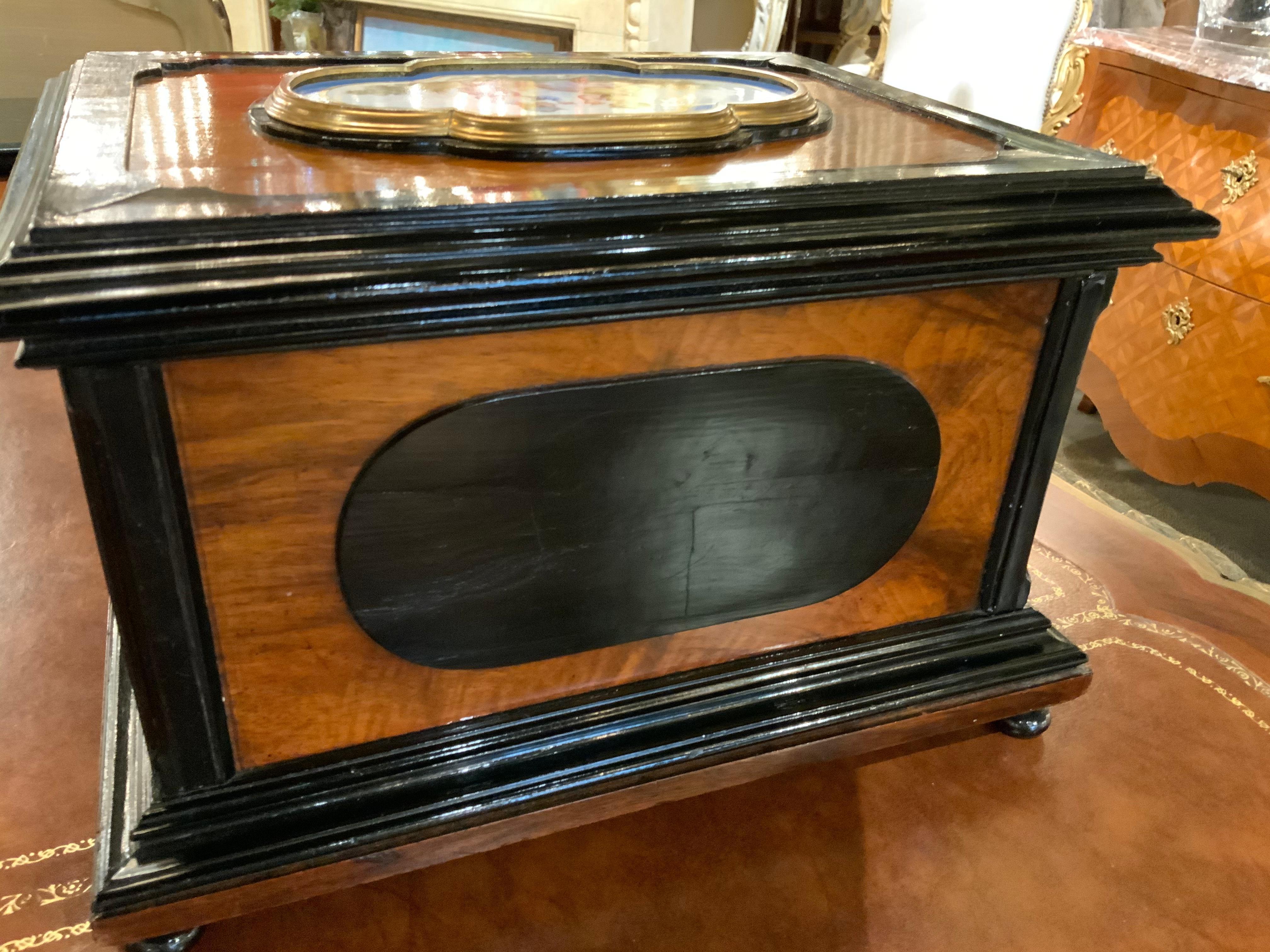 Walnut veneered case with ebonized trim and set with Sevres-style polychrome plaques decorated
With children and trophies, set into brass bezels, the interior fitted as a jewelry box.