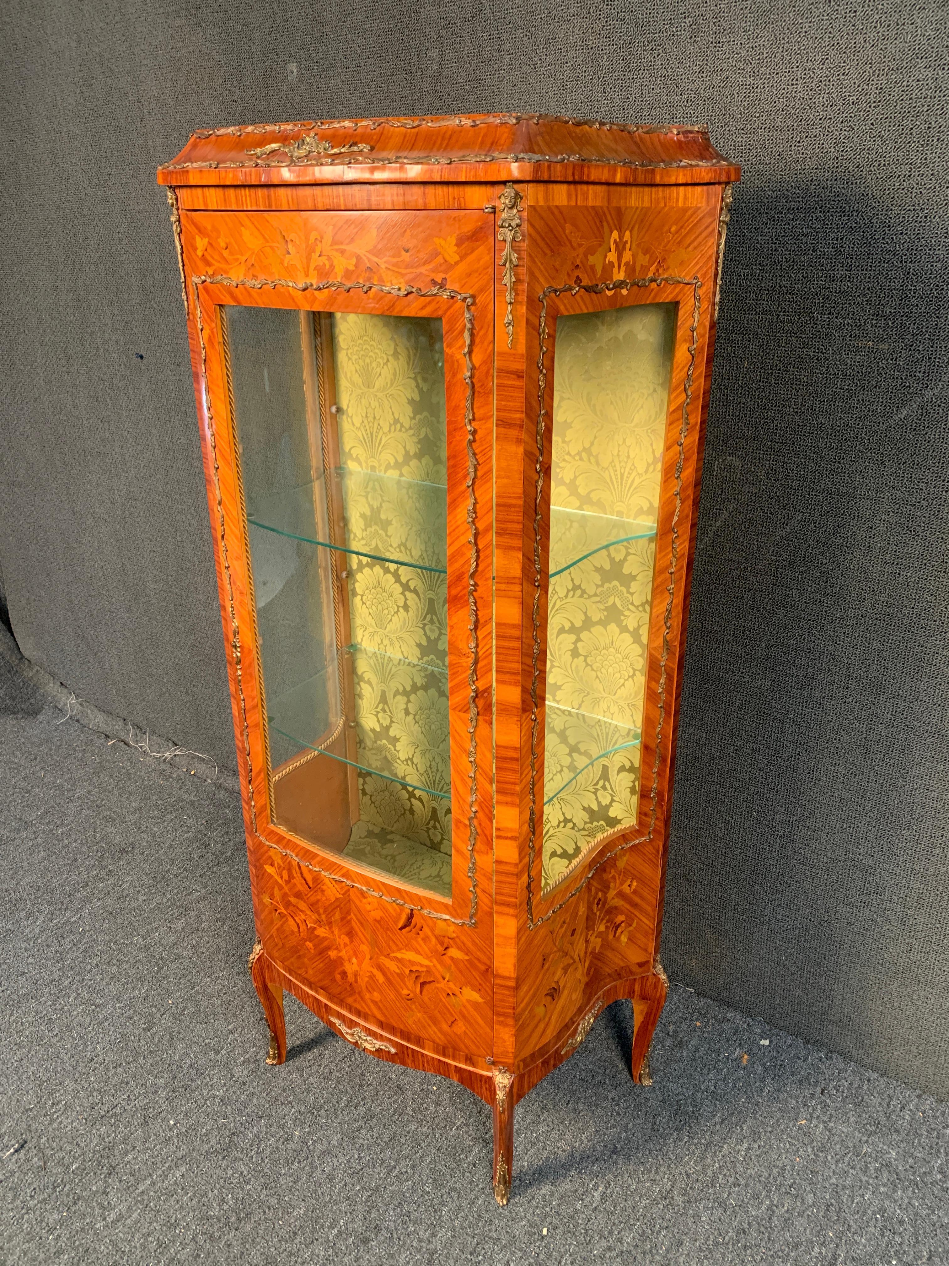 For your consideration a exquisite late 19th century French Louis XVI style kingwood vitrine featuring gilded ormolu accent mounts, shaped glass front panels and glass shelving , lined floral fabric within, foliate marquetry inlay to the door