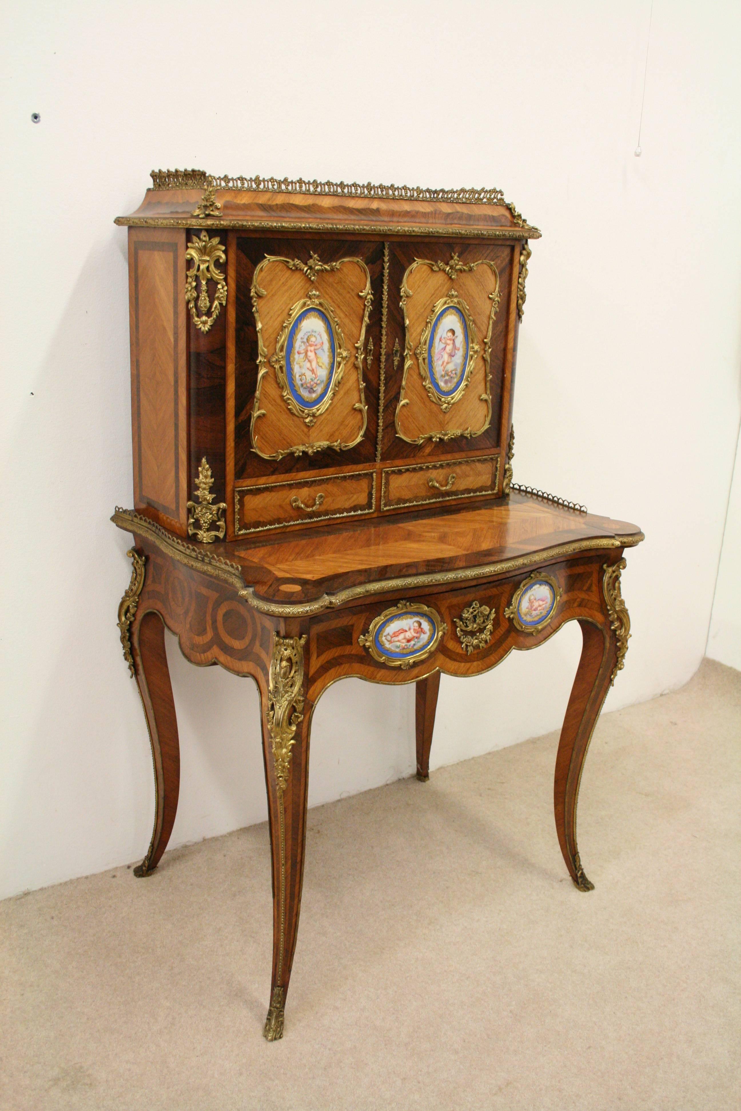 French kingwood, rosewood and porcelain mounted Bonheur du jour, circa 1860. The raised top with pierced three-quarter gallery above a pair of panel doors outlined with gilt-metal and enclosing a pair of Sèvres style panels depicting winged putti,