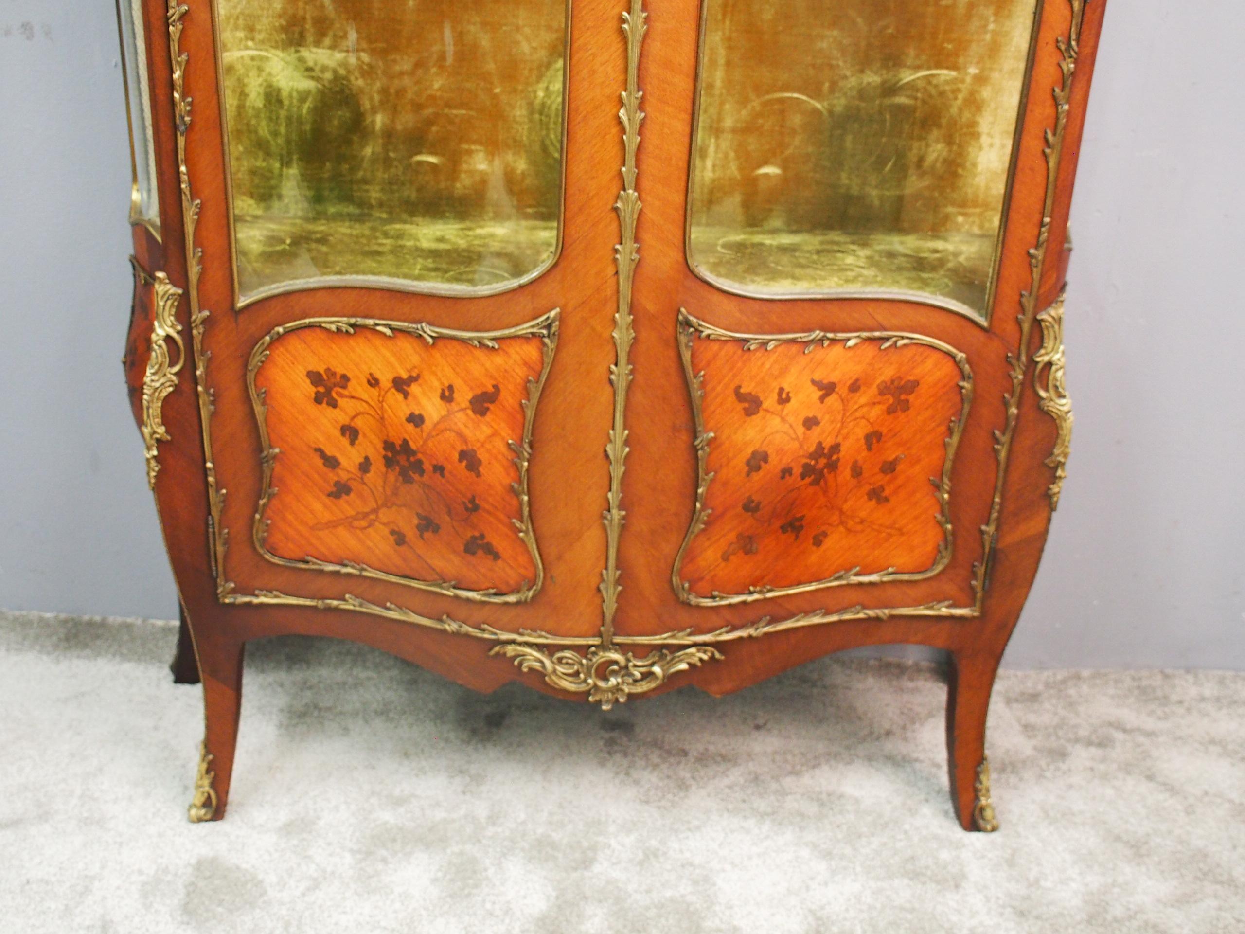 French, serpentine-fronted, ormolu mounted kingwood and walnut display cabinet. The domed top is surmounted by a Rococo ormolu cartouche over an ormolu mounted side glazing and the doors show the velvet-lined interior with glazed shelving. The lower