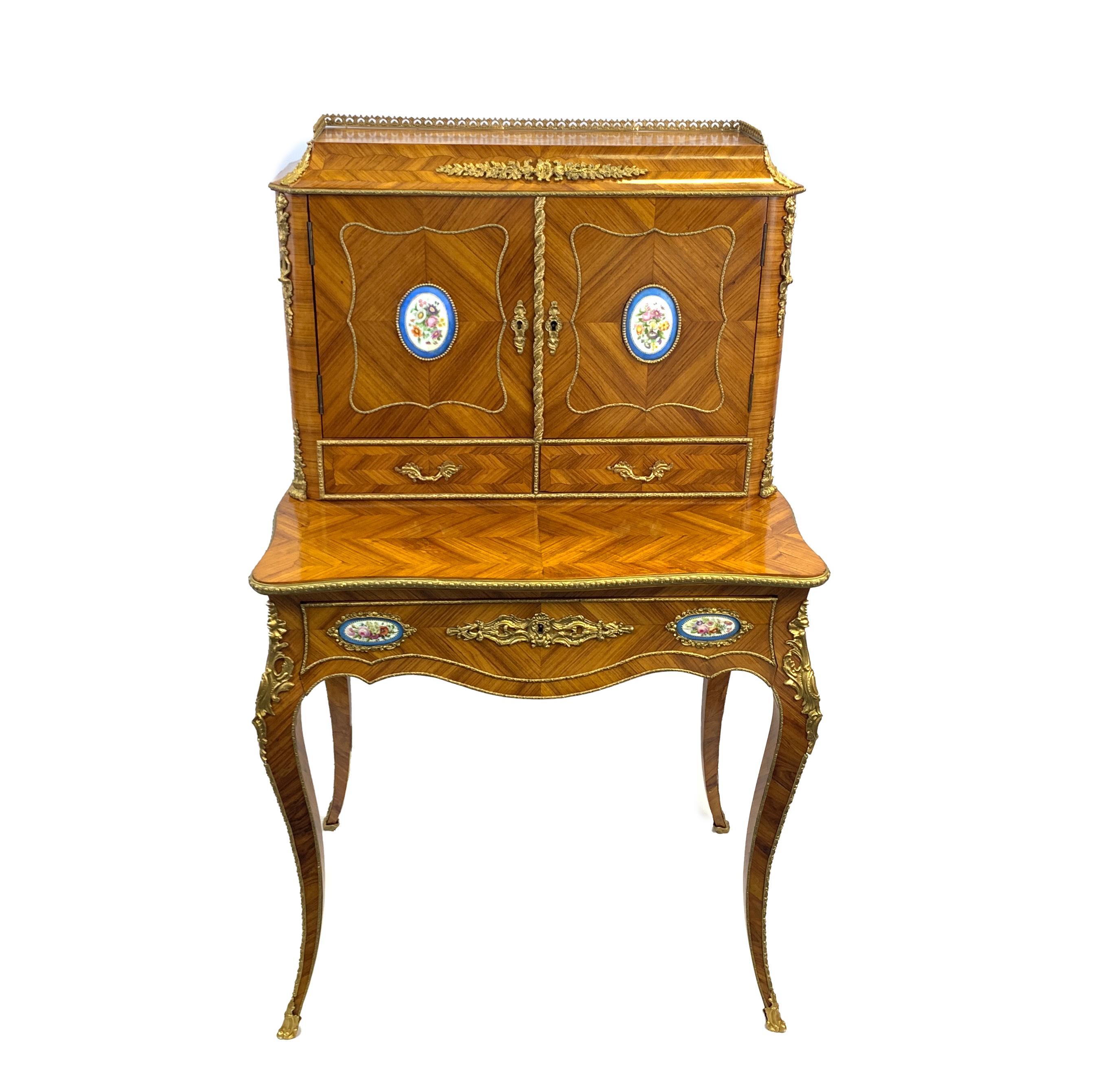 A late 19th century French kingwood, gilt metal and porcelain mounted Bonheur du jour, with quarter veneered panels in crossbanded surrounds, the upper part with a cavetto top, applied floral foliage and pierced three quarter gallery, enclosed by a