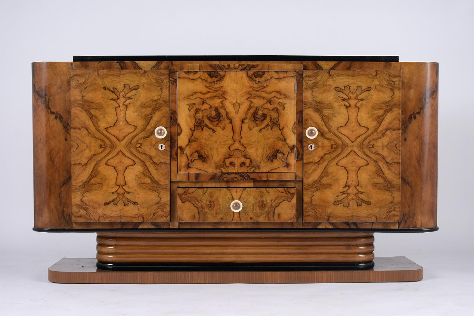 This French Art Deco buffet has been restored and has a walnut and black color combination with a lacquered finish. The buffet features an exotics walnut veneers, flat wooden top, two curved sides, and a center door pushes to open, and single