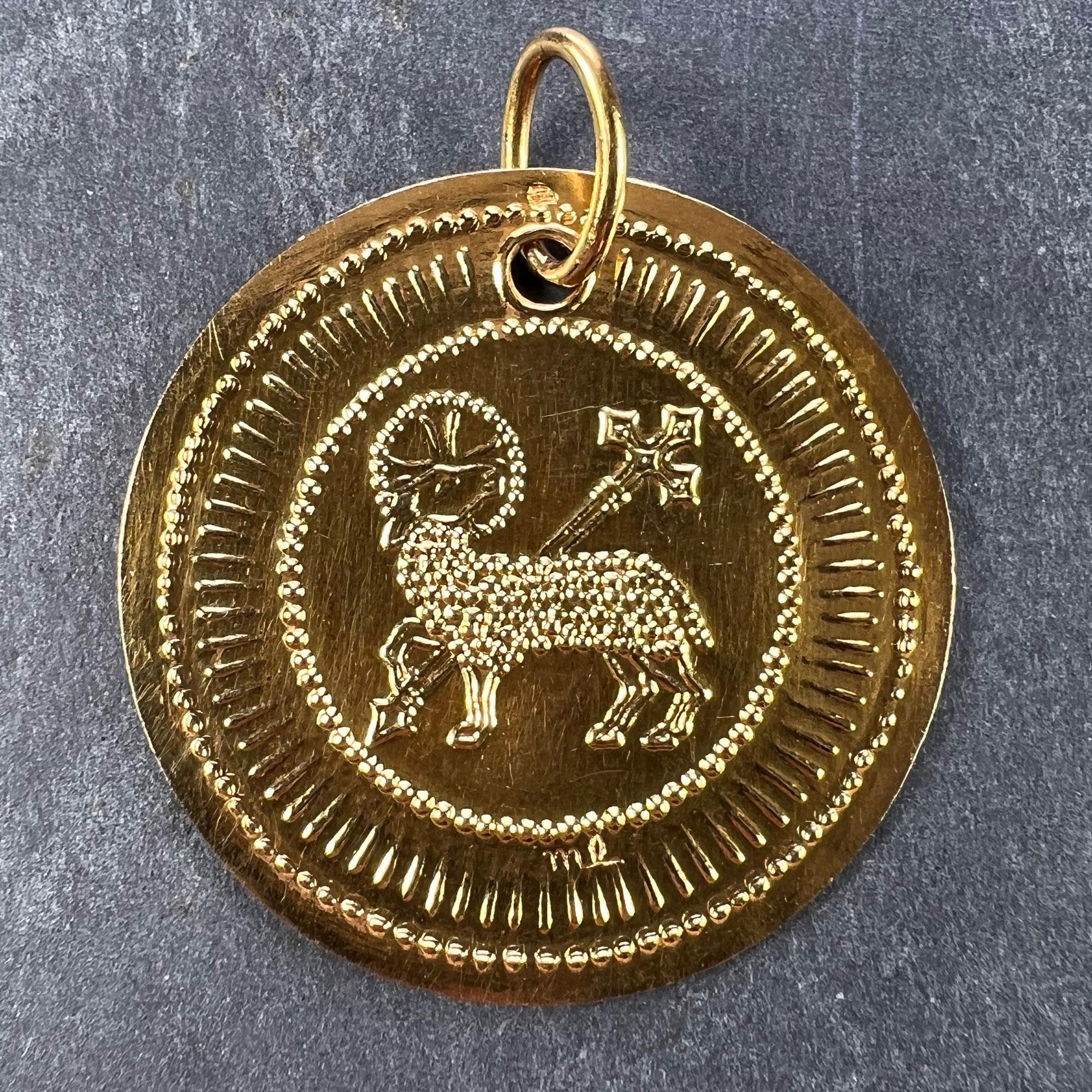 A French 18 karat (18K) yellow gold pendant designed as a round medal with a depiction of the Lamb of God with a sceptre surmounted by a cross to the centre surrounded by a radiant design of dots and lines. Stamped with the eagle's head for French