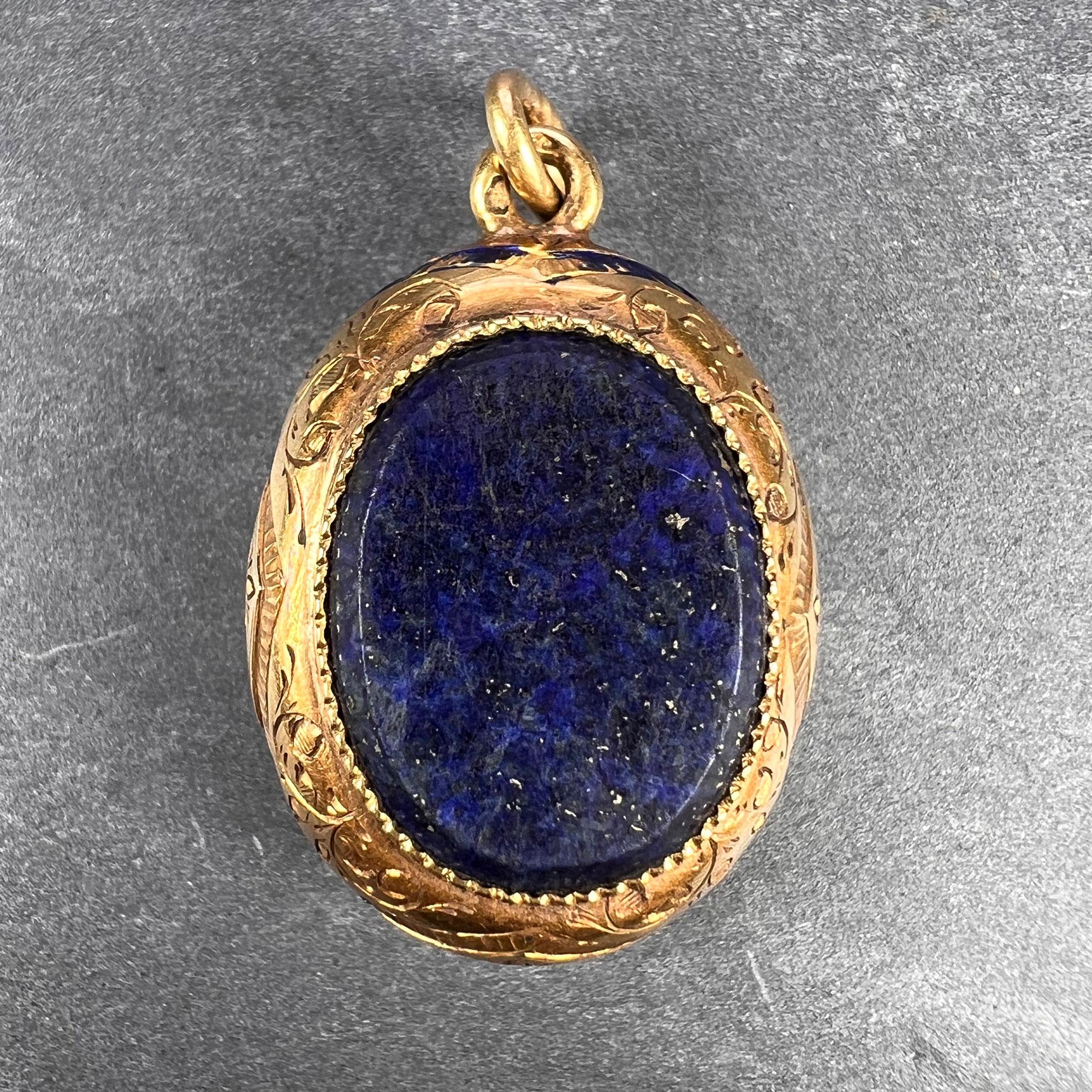 Pendentif de charme en or jaune 18 carats (18K) de fabrication française, conçu comme un cadre ovale à décor gravé et traces d'émail bleu, serti de chaque côté d'une tablette ovale en lapis-lazuli. Estampillé de la marque de l'aigle pour l'or 18