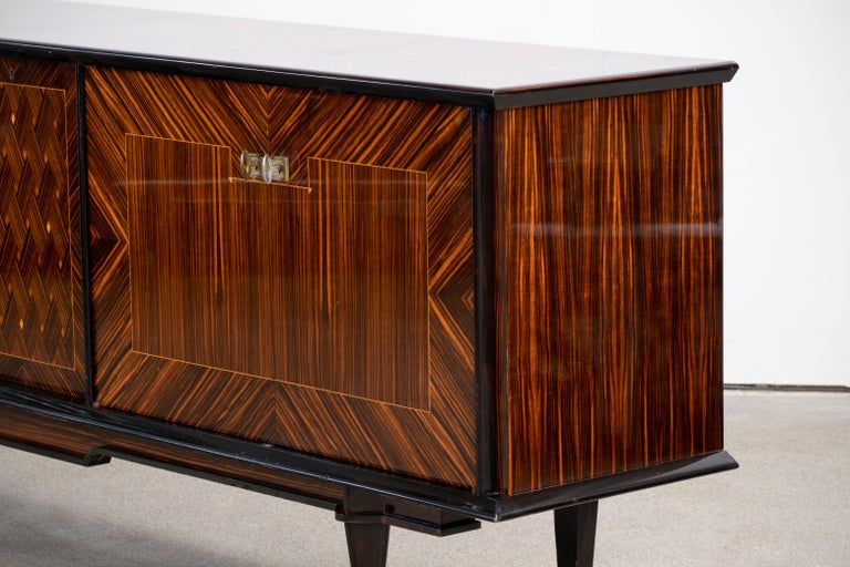 French Art Deco sideboard, credenza. The sideboard features stunning Macassar wood grain with a geometric pattern in the center. It offers ample storage, with shelve behind the doors. Both sides of the cabinet lock, and two keys are included. The